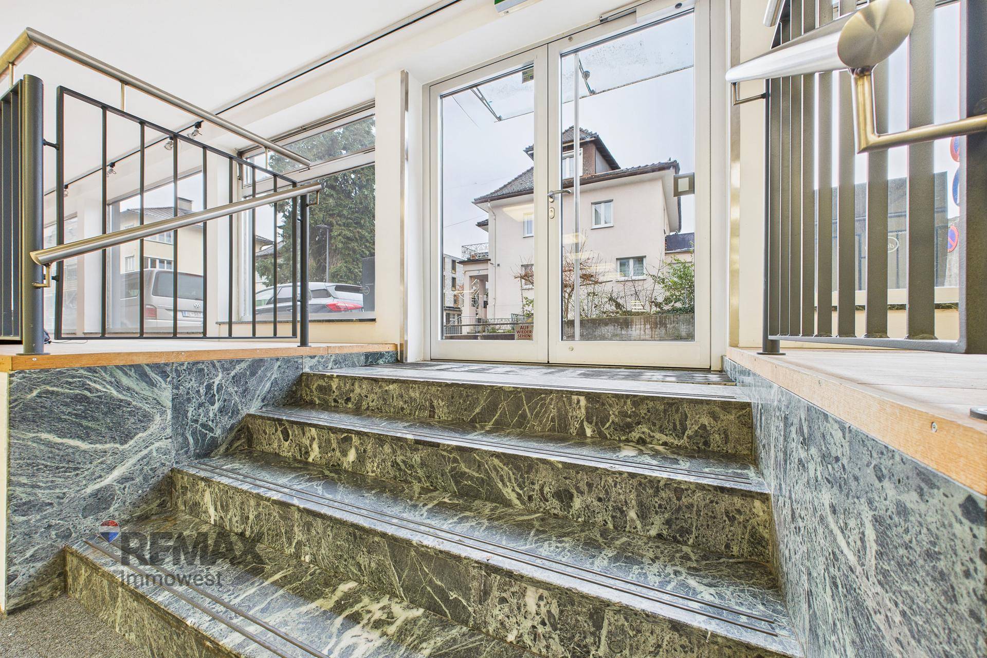 Heller Eingangsbereich mit Marmortreppe und großen Glastüren, die Tageslicht hereinlassen.