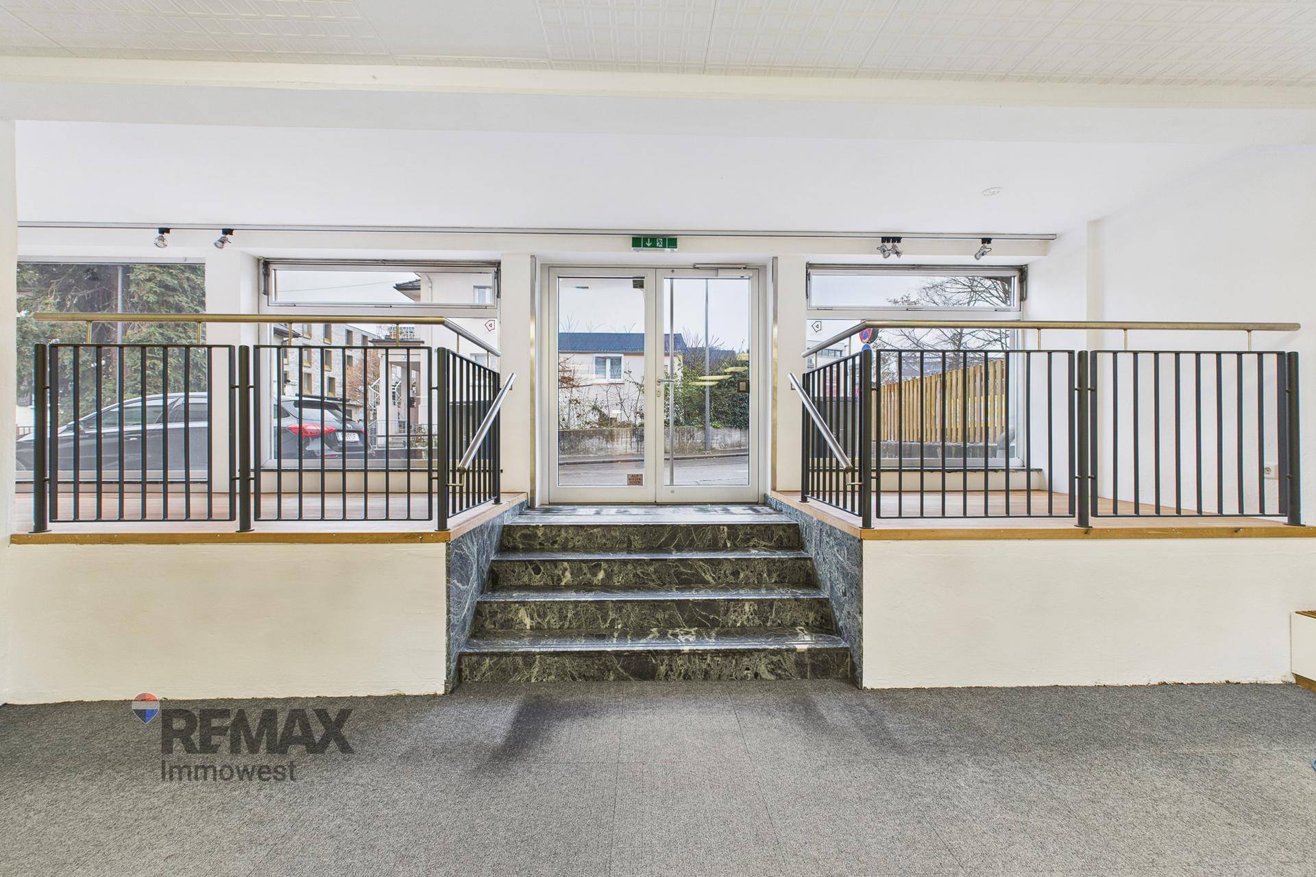Geräumiger Eingangsbereich mit Marmortreppe, Glastüren und Teppichboden, der zum Hauptraum führt.