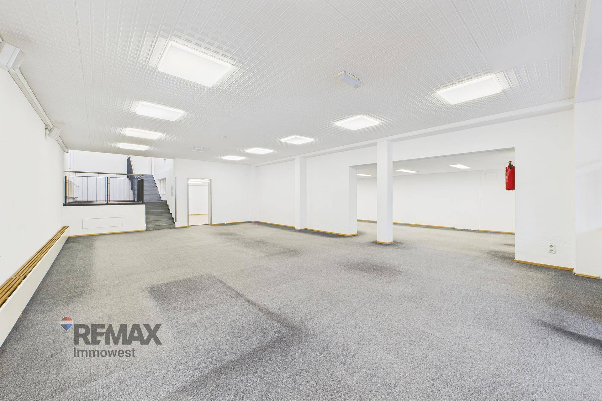 Weitläufiger, heller Geschäftsraum mit grauem Teppichboden, weißen Wänden und moderner Deckenbeleuchtung.