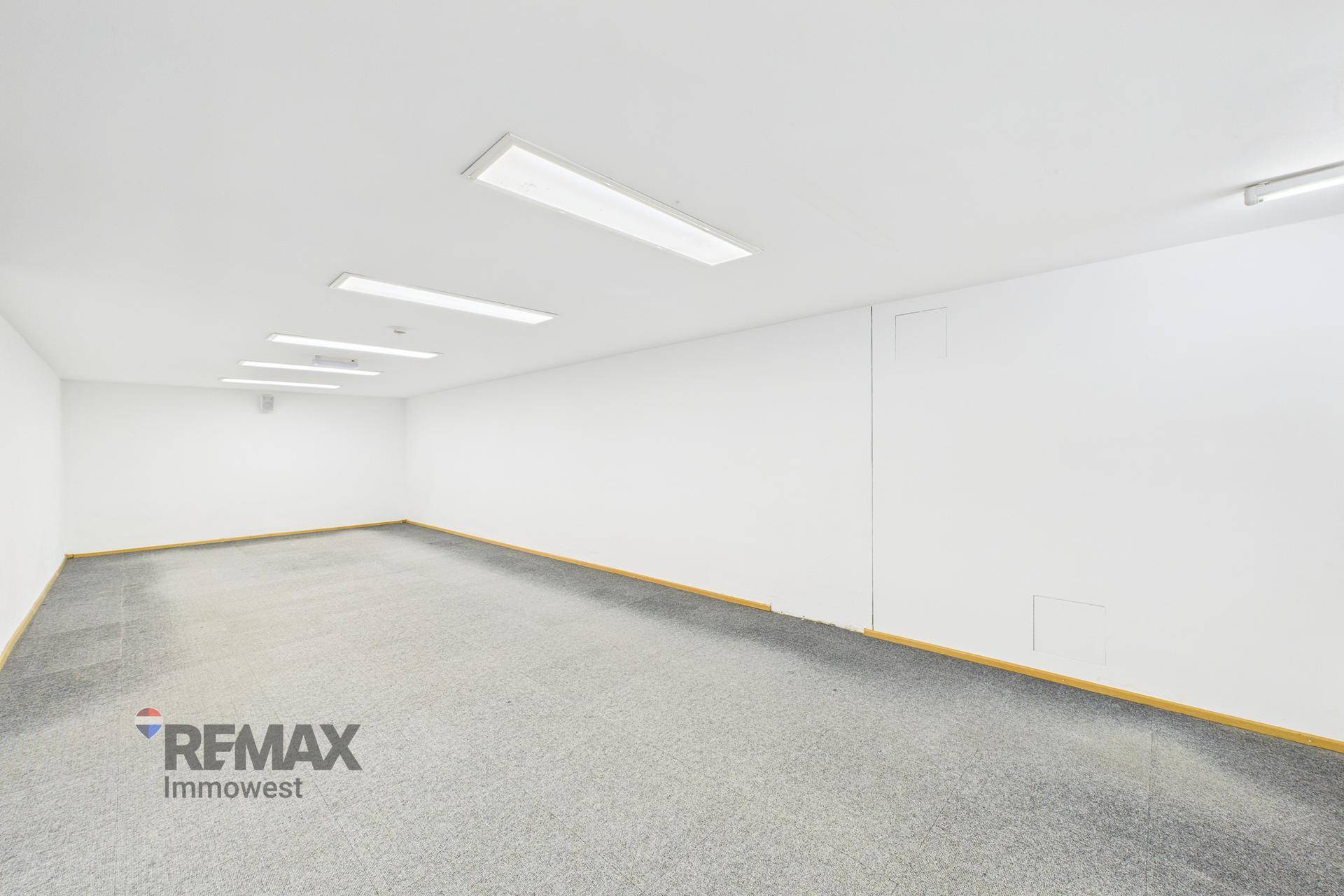 Langer, schmaler Gewerberaum mit Teppichboden und effizienter Deckenbeleuchtung.