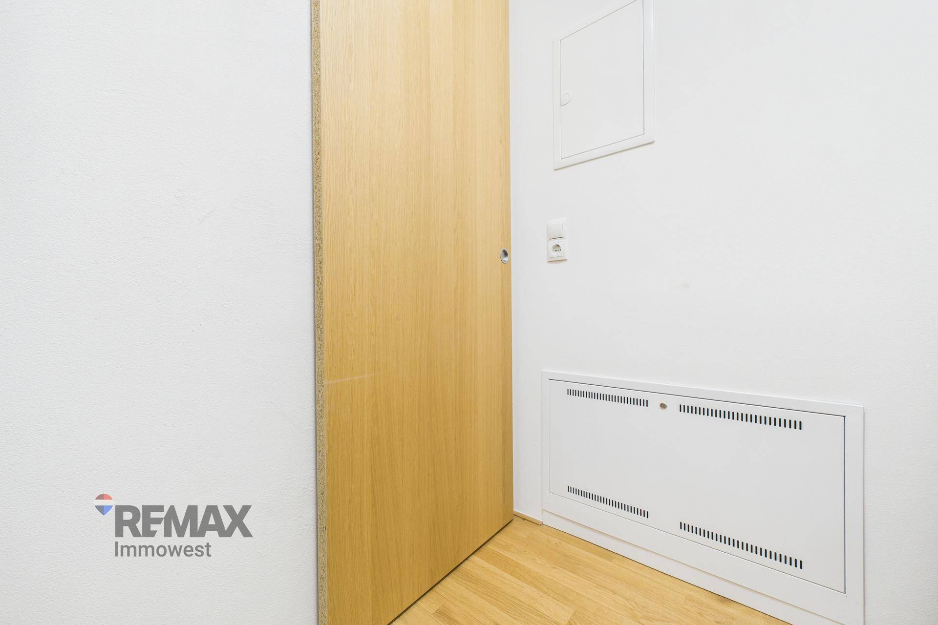 Innenraum mit Holztür und einem Heizungs- oder Technikpanel an der Wand.