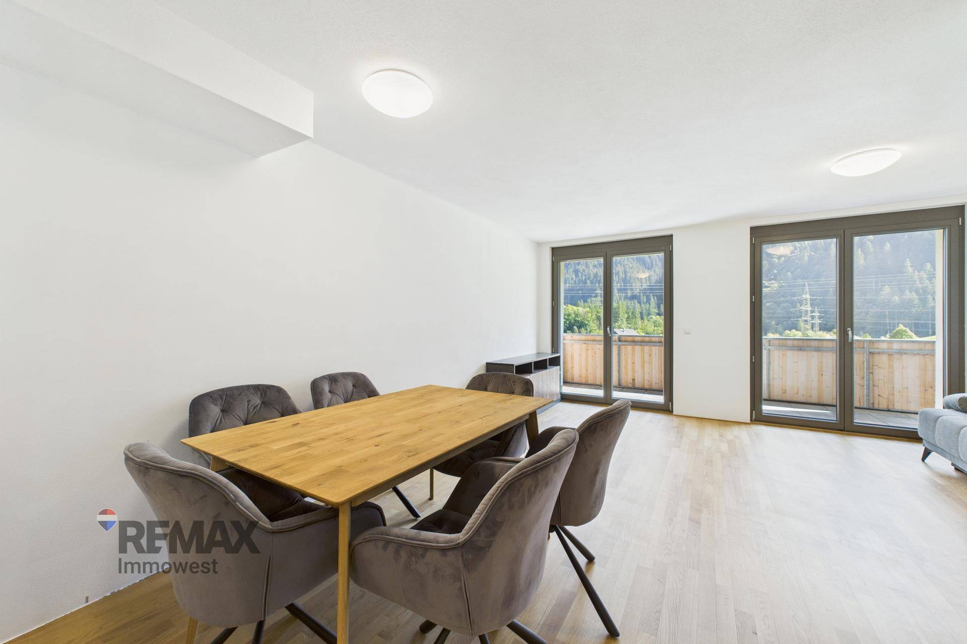 Geräumiger Wohn- und Essbereich mit Holzboden und großen Fenstertüren, die auf einen Balkon führen.