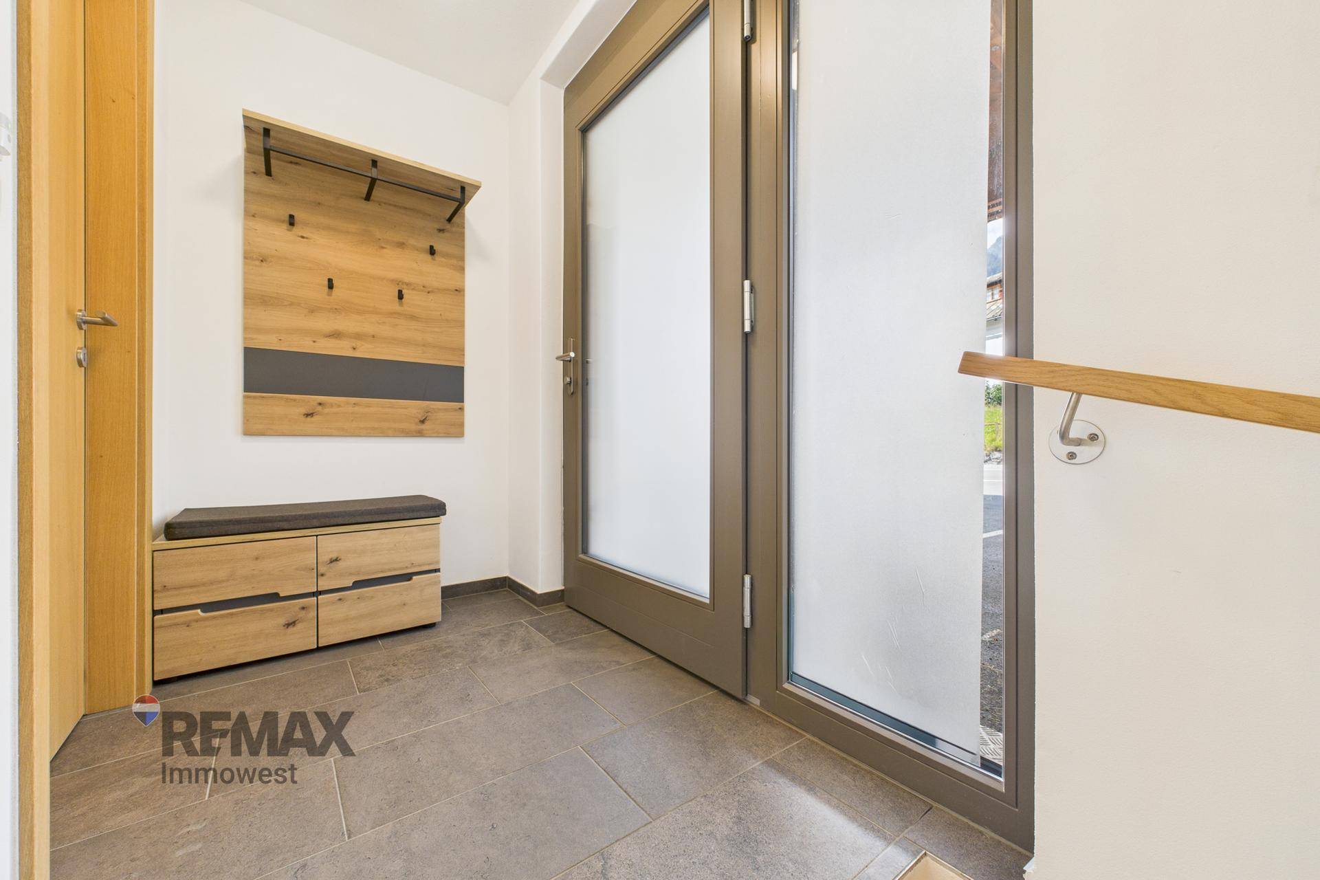 Heller Eingangsbereich mit Fliesenboden, Garderobe und einer modernen Haustür mit Milchglas.