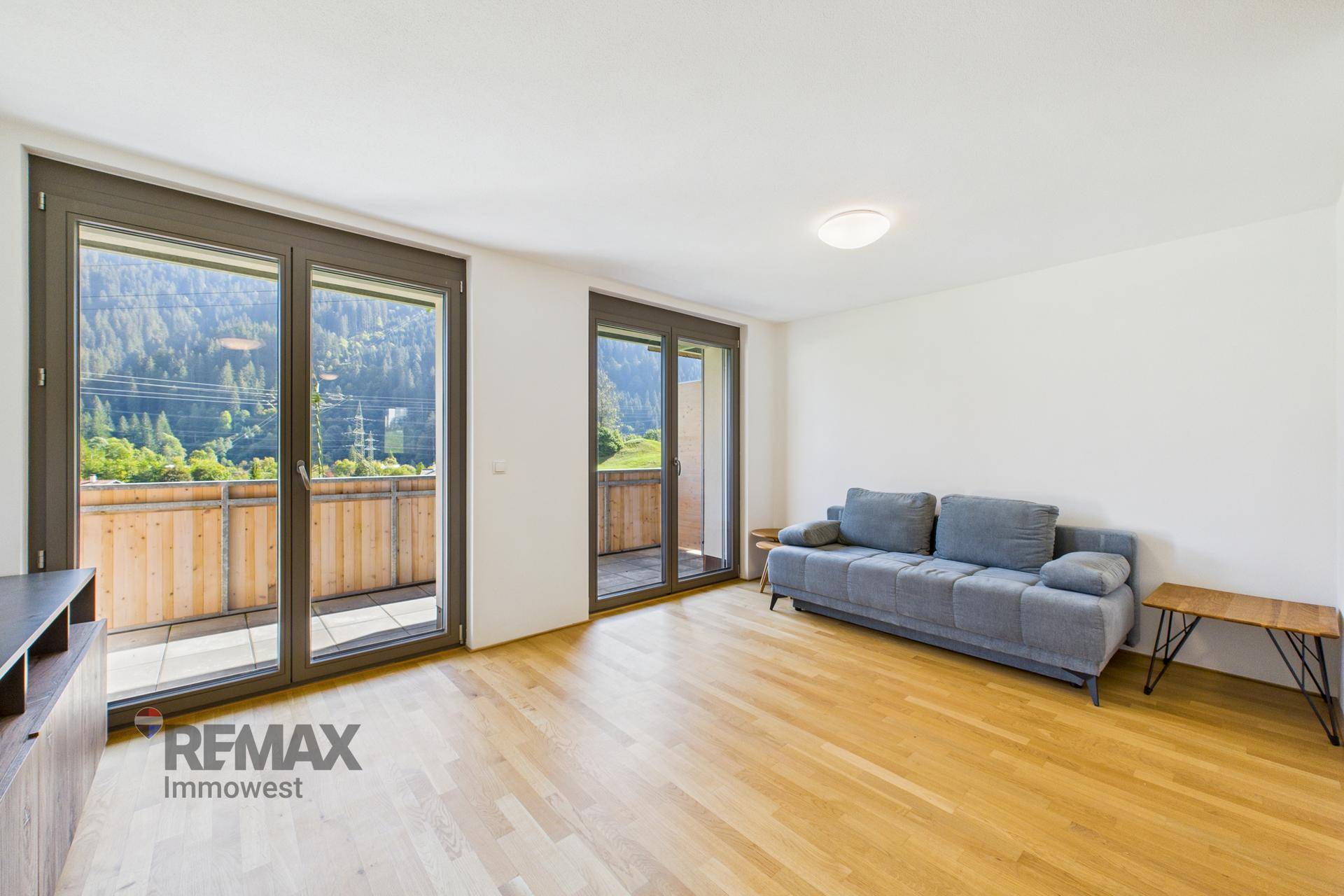 Helles Wohnzimmer mit bequemer Couch, Holzboden und großen Fenstertüren zum Balkon.