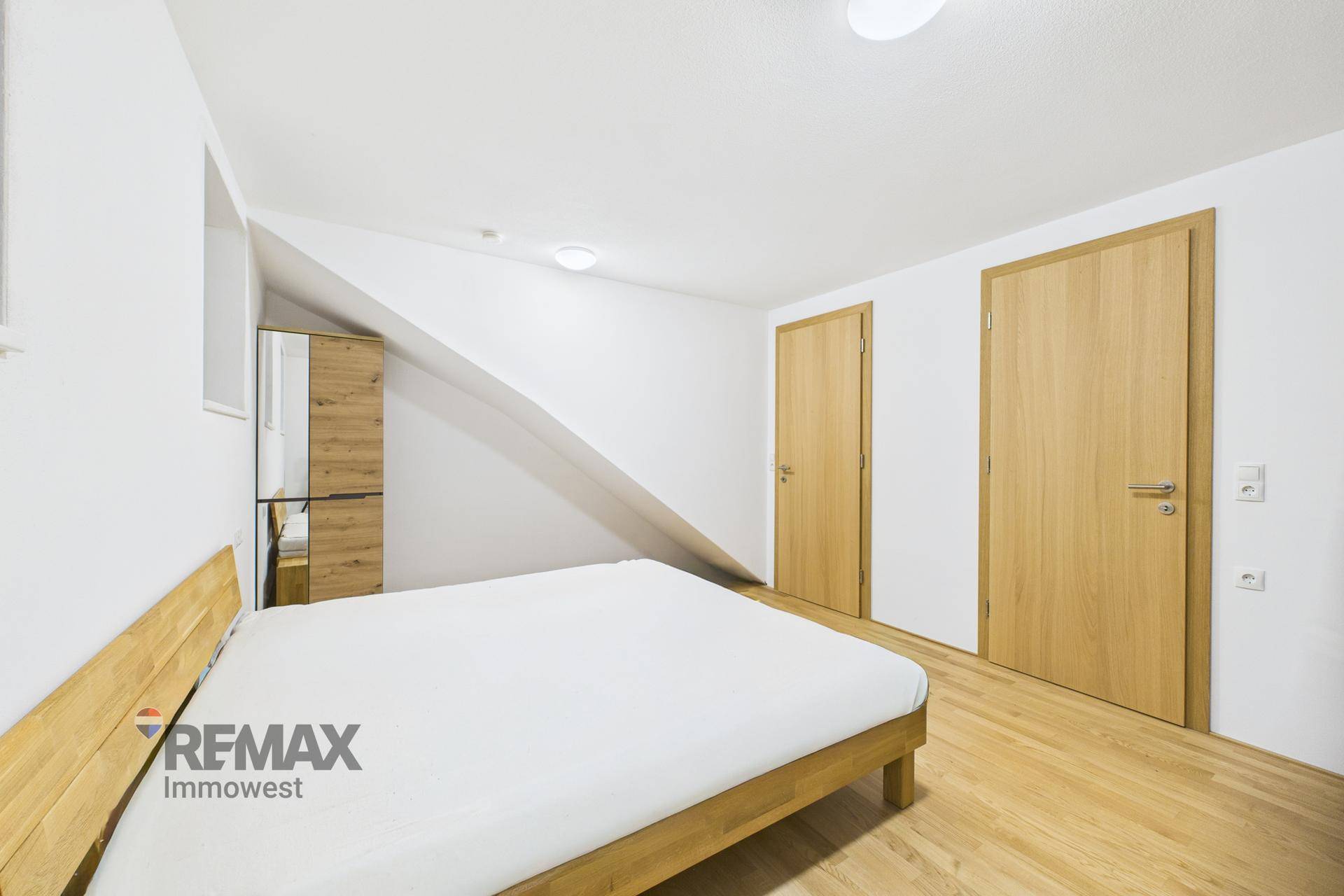 Gemütliches Schlafzimmer mit Holzboden, Dachschräge und zwei Holztüren, die den Raum ergänzen.