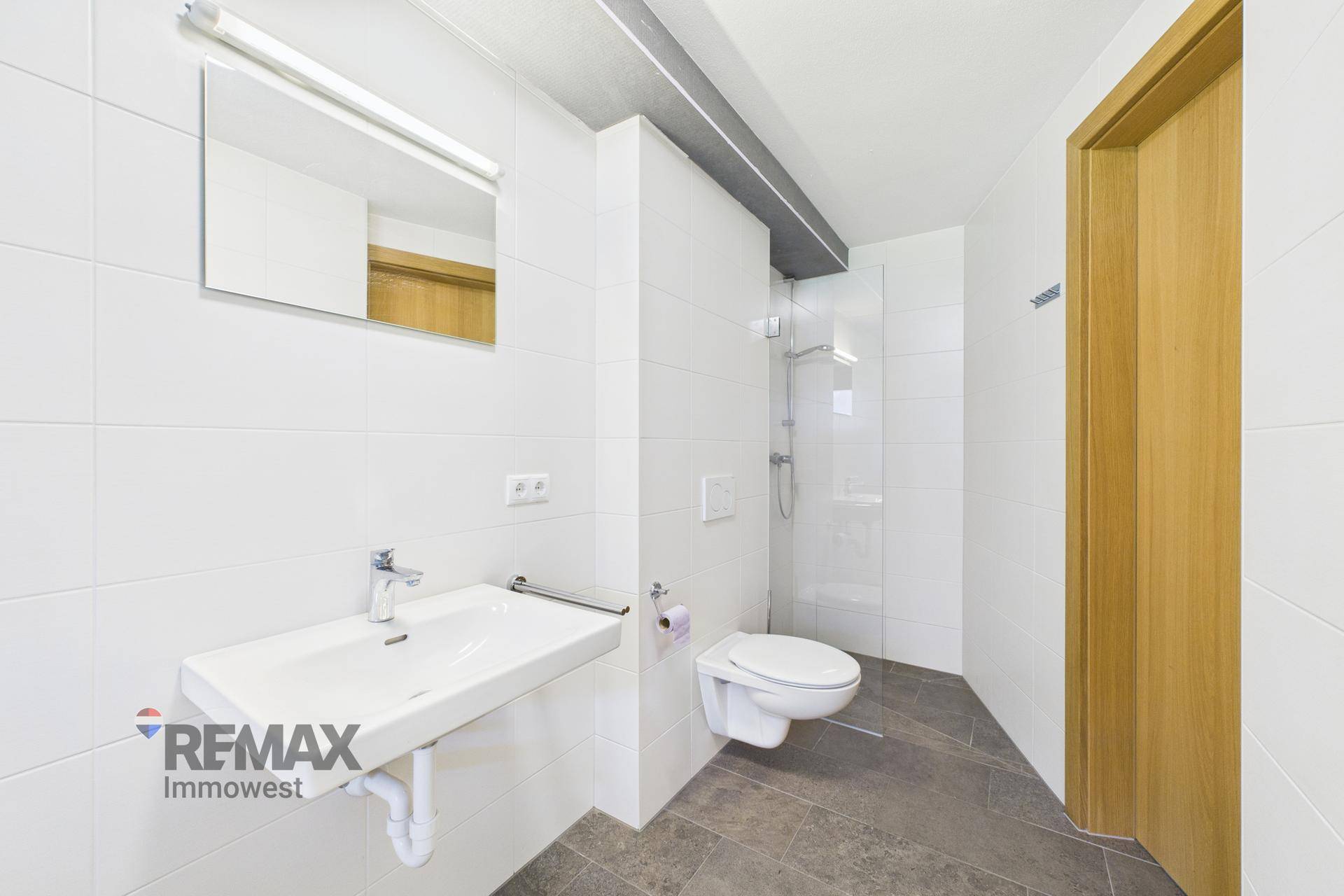 Modernes Badezimmer mit weißen Fliesen, wandhängendem WC und einer begehbaren Dusche.