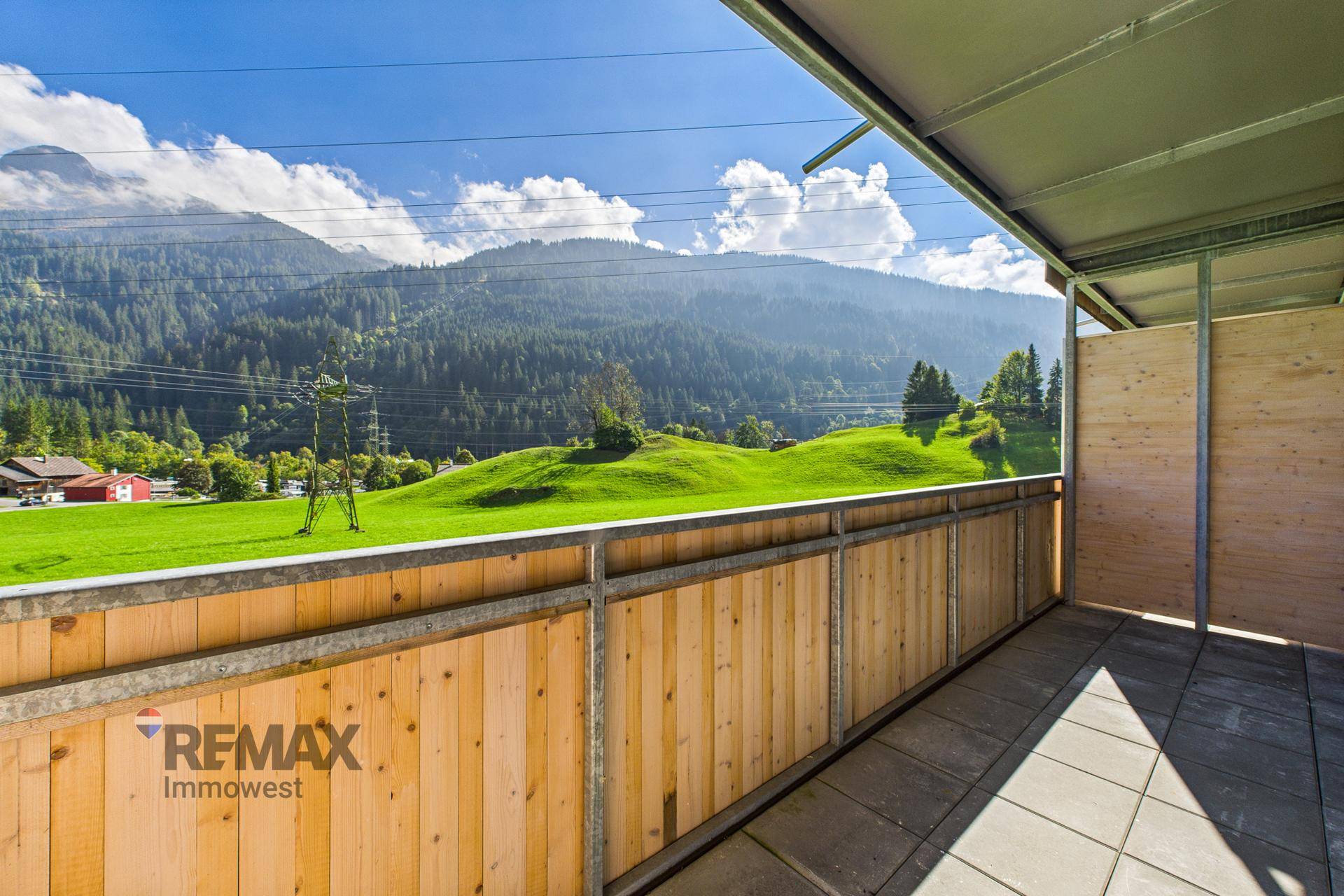 Geräumiger Balkon mit Holzelementen und weitem Blick über grüne Wiesen und Berge.