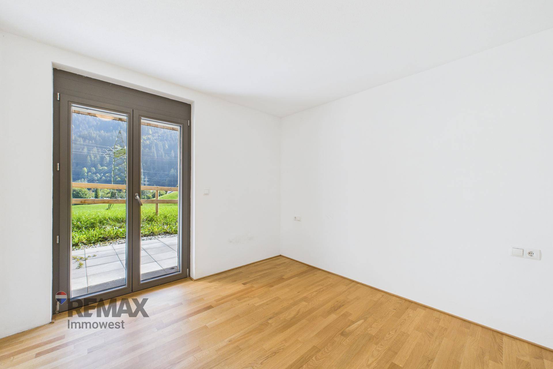 Helles Zimmer mit Holzboden und großer Fenstertür, die Zugang zu einer Terrasse bietet.