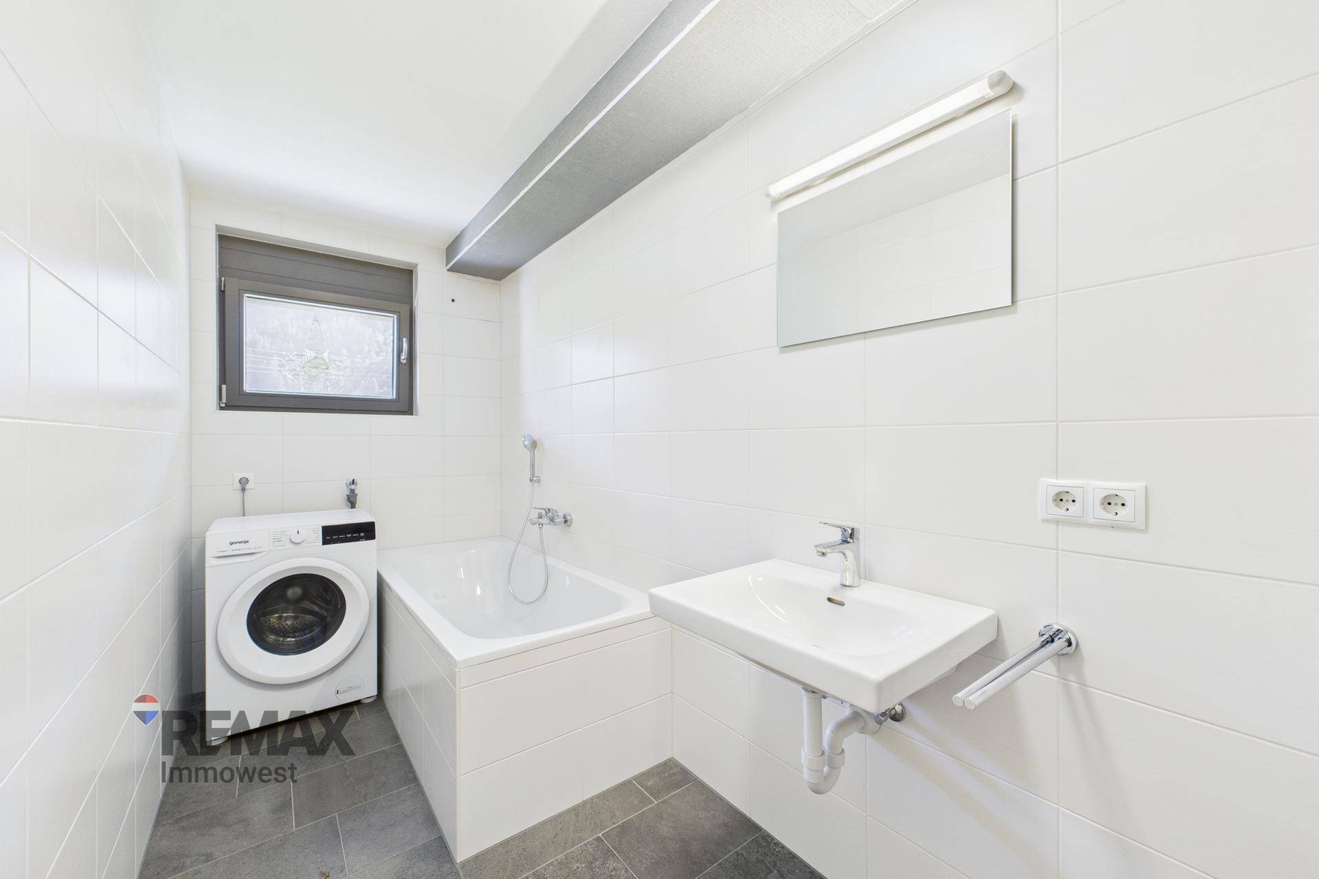 Helles Badezimmer mit Badewanne, Waschmaschine und Fenster für natürliche Belüftung.