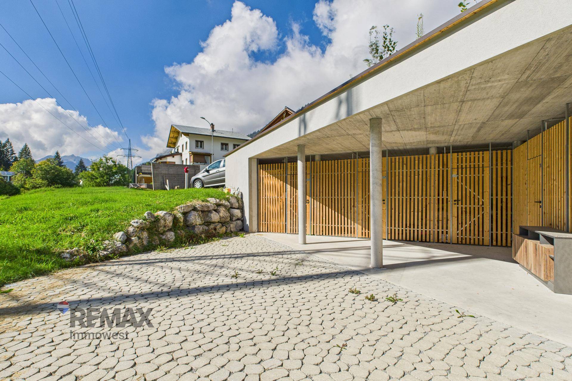 Moderne Tiefgarage mit Holzlamellen und gepflasterter Zufahrt, umgeben von Grünflächen.