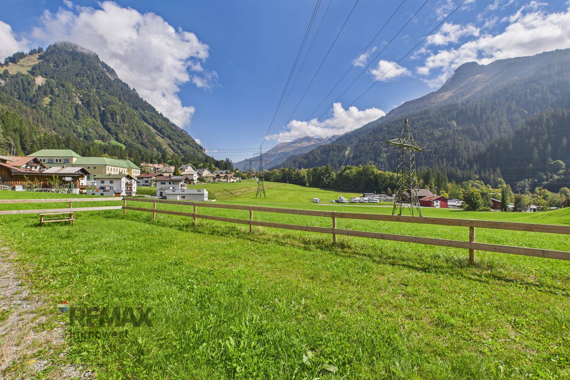 Weitläufige grüne Wiese mit Holzzaun und beeindruckendem Panoramablick auf die Berge.