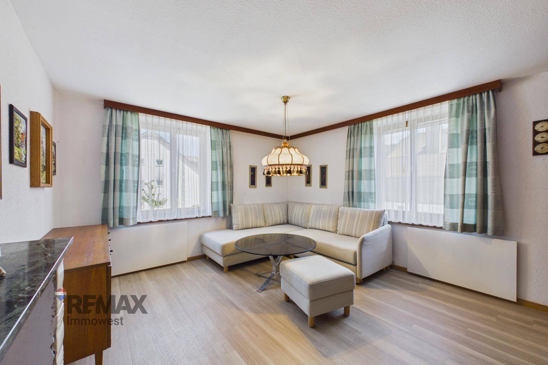 Gemütliches Wohnzimmer mit Ecksofa, großem Fenster und hellem Laminatboden, ideal zum Entspannen.