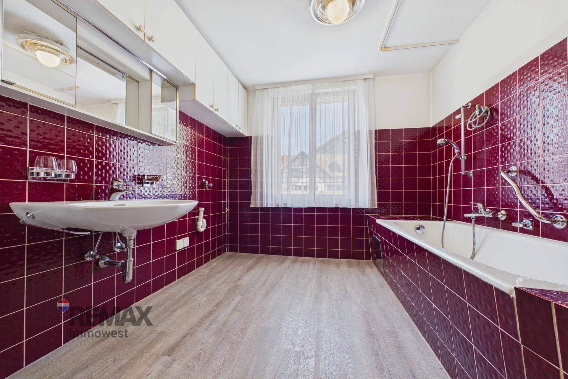 Badezimmer mit roten Fliesen, Badewanne, Waschbecken und Fenster, in gutem Zustand.