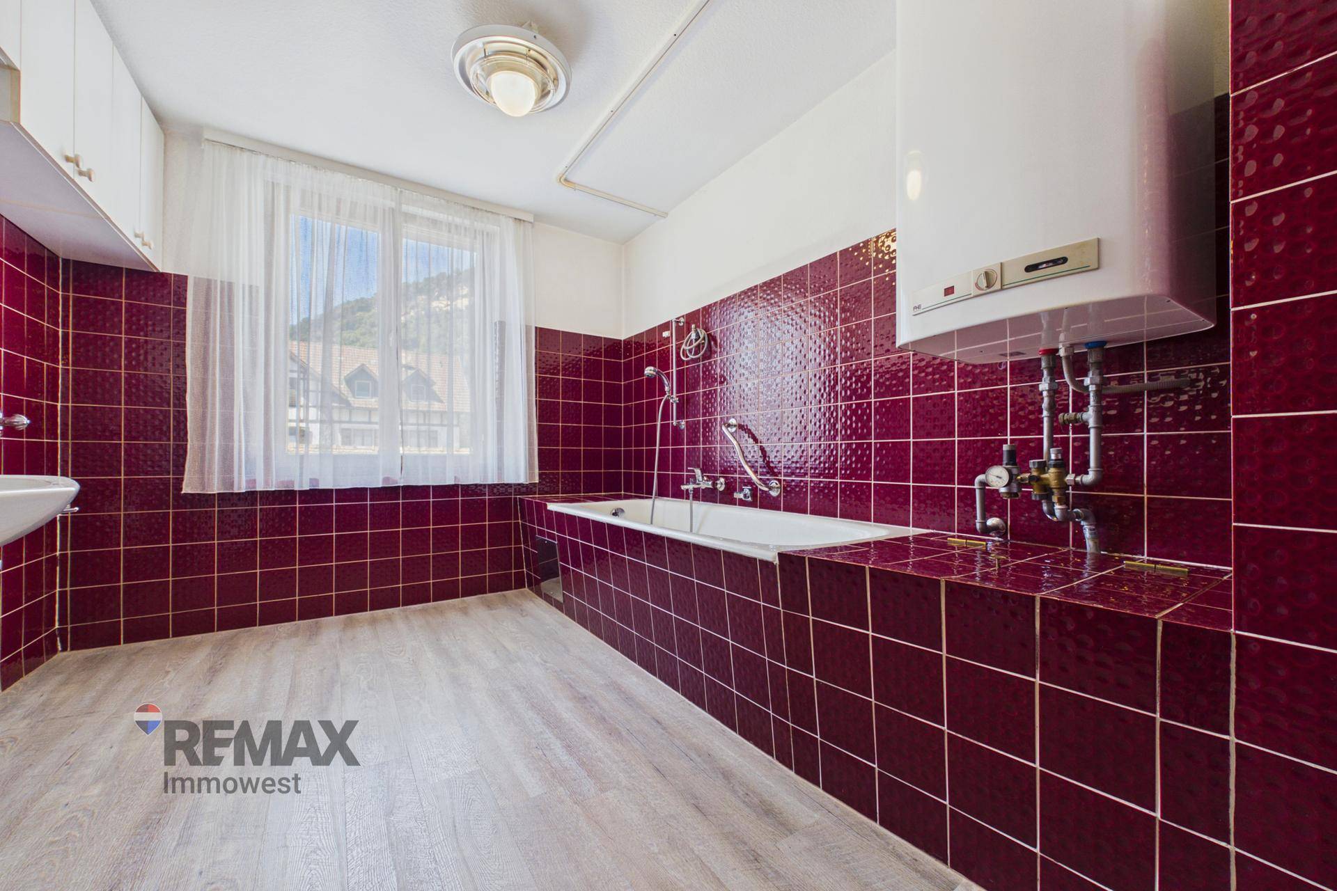Badezimmer mit roten Fliesen, Badewanne und Warmwasserboiler an der Wand, funktional und sauber.