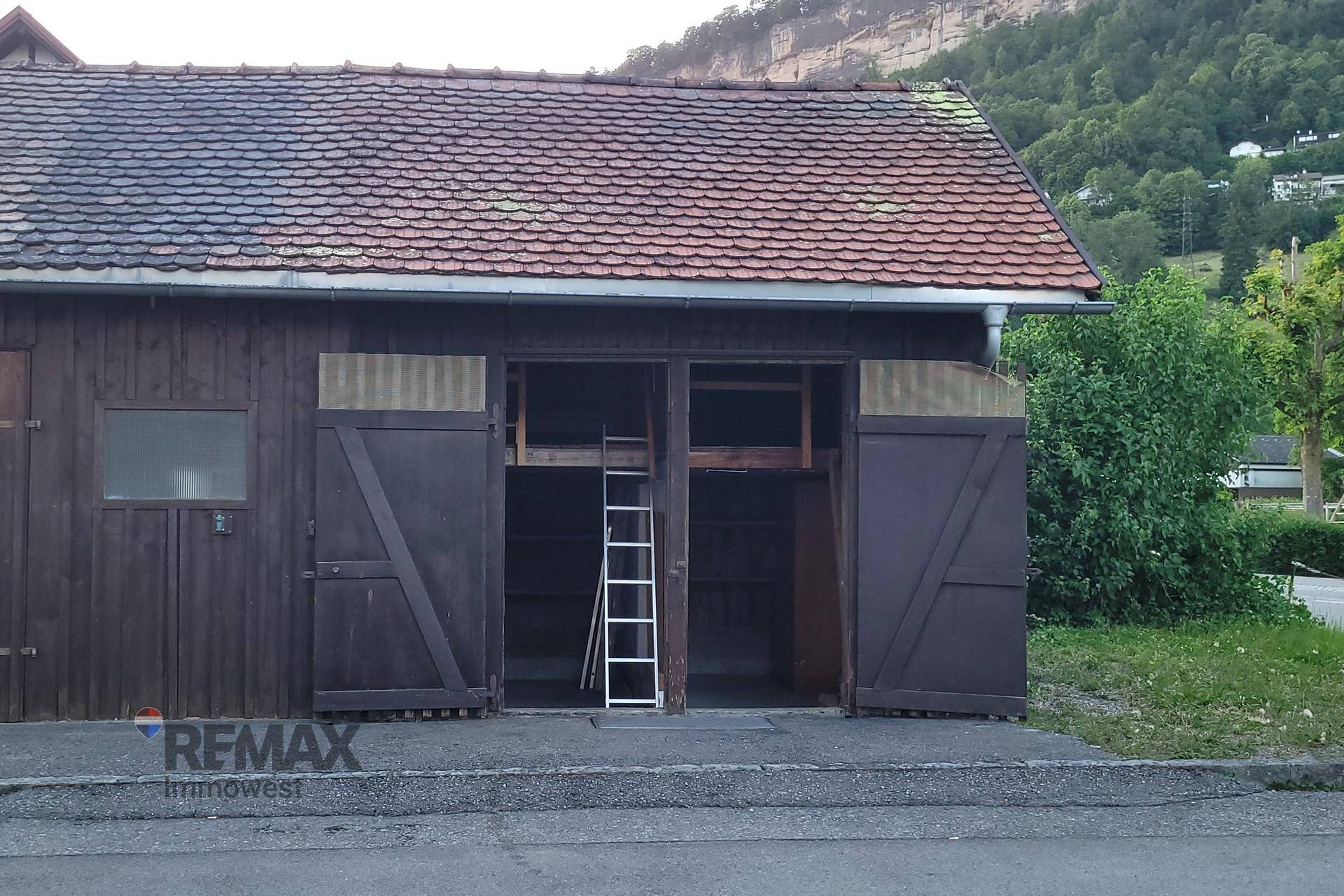 Rustikale Holzscheune mit großem Tor und Ziegeldach in ländlicher Umgebung, bietet viel Stauraum.