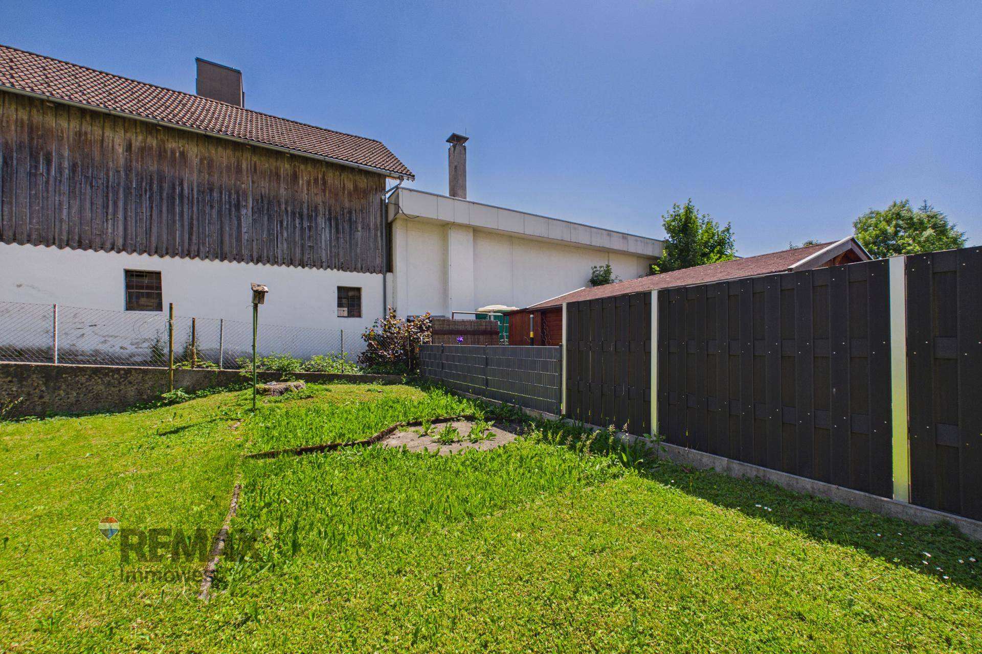 Grüner Gartenbereich mit Rasenfläche und Zaun, umgeben von Gebäuden, bietet Platz im Freien.