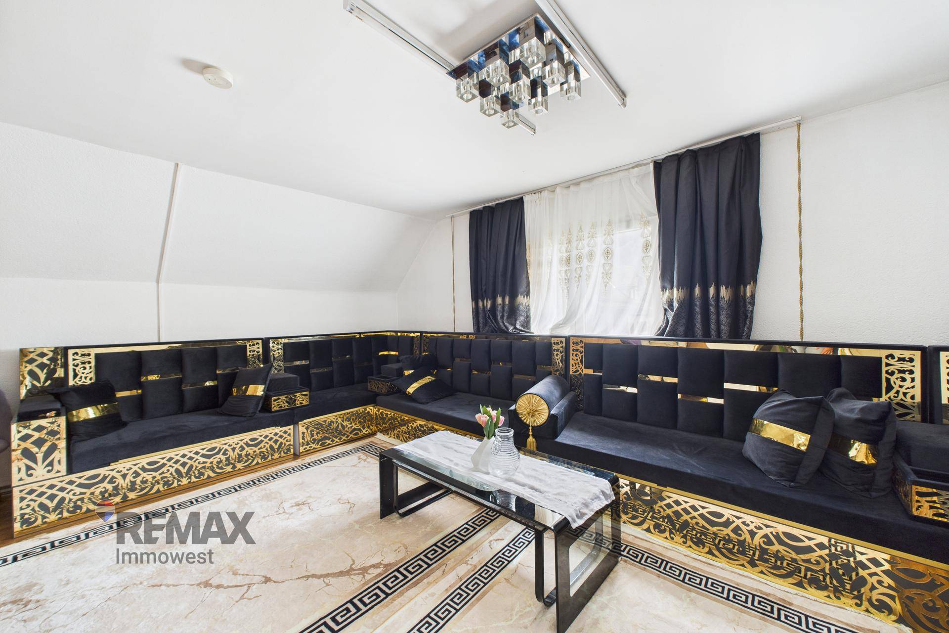 Luxuriöses Wohnzimmer mit dunklen Samtsofas, goldenen Akzenten und Dachschräge.