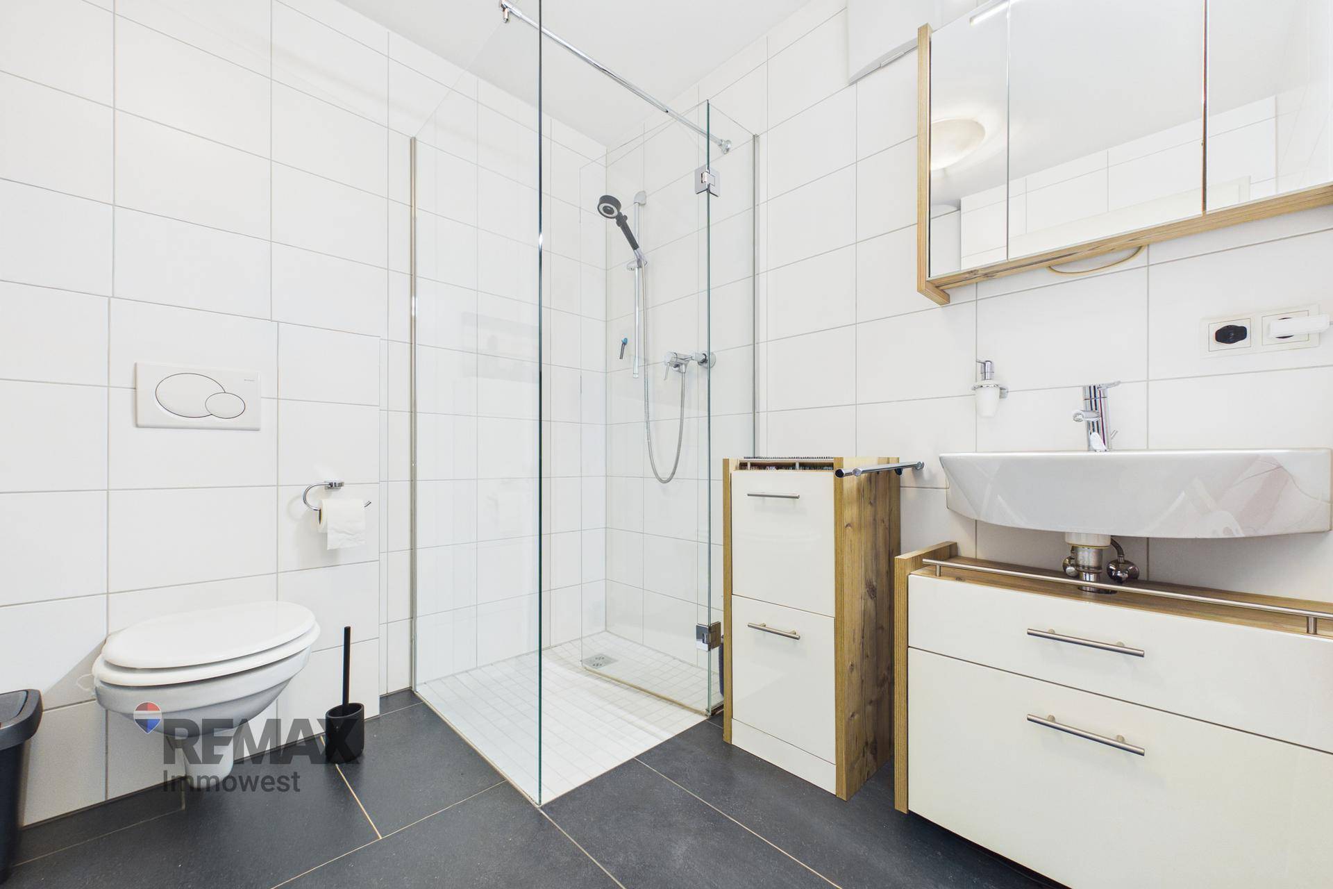 Modernes Badezimmer mit ebenerdiger Glasdusche, WC und Einzelwaschbecken mit Holzunterschrank.