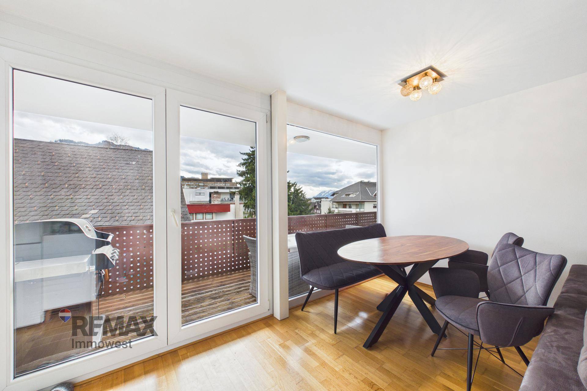 Heller Wohn-Essbereich mit Zugang zum Balkon durch große Fenster und Holzboden.