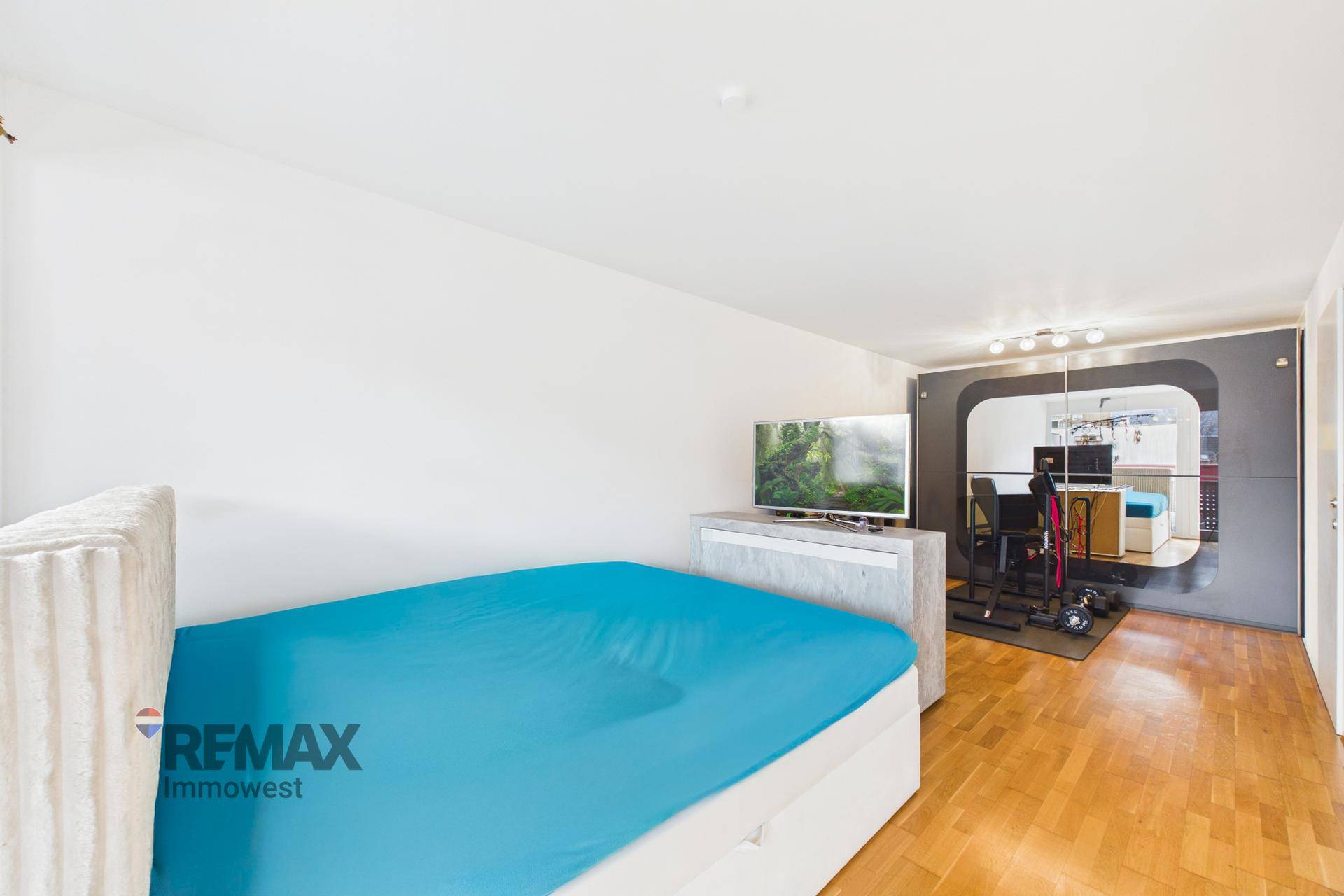 Schlafzimmer mit Holzboden, Bett und integriertem Fitnessbereich mit Spiegelwand.