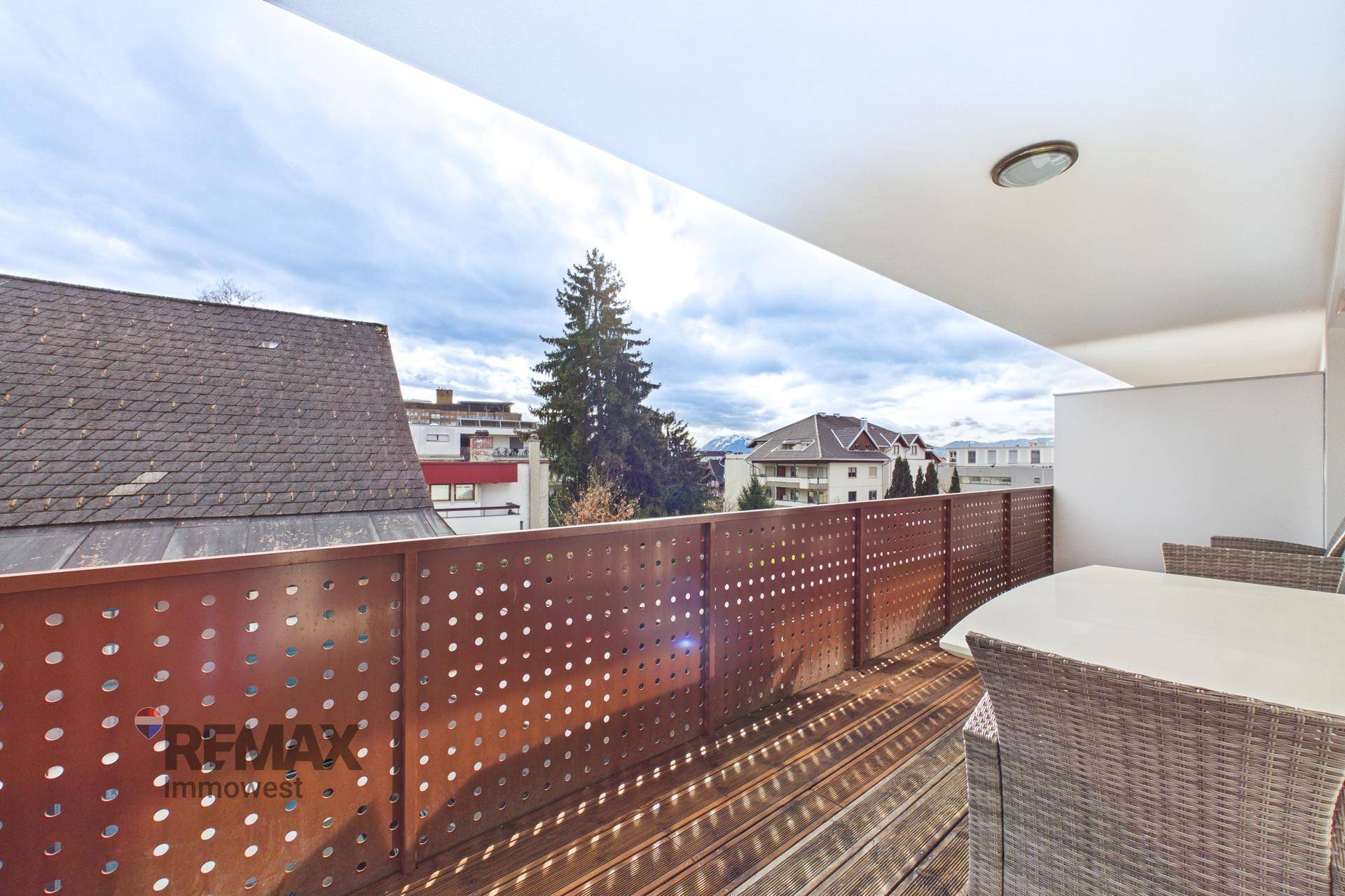 Geräumiger Balkon mit Holzboden, Sitzgelegenheiten und Blick auf die umliegende Bebauung.
