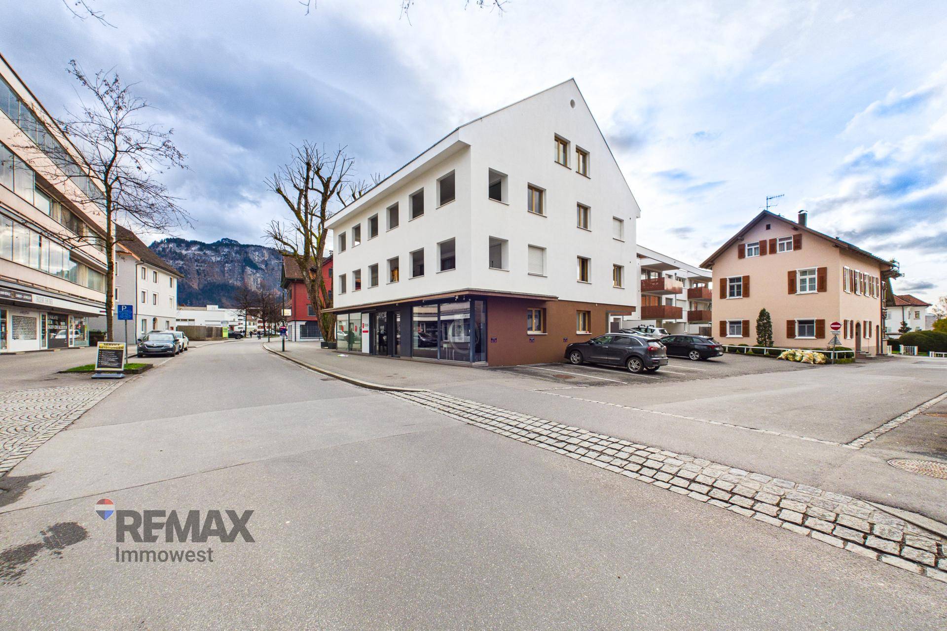 Straßenansicht mit Wohn- und Geschäftsgebäuden in urbaner Umgebung und Bergblick.