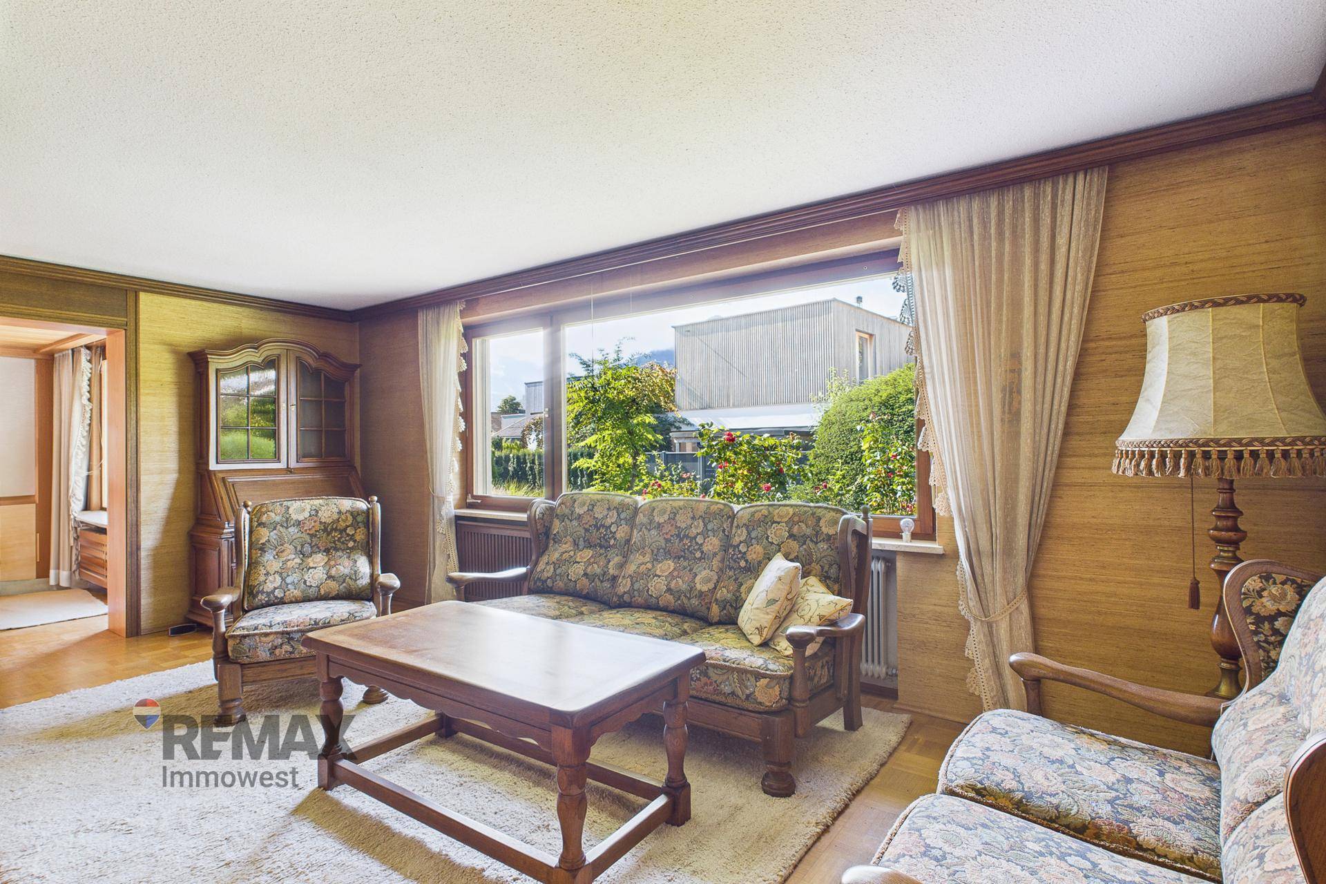 Gemütliches Wohnzimmer im Vintage-Stil mit floralen Sofas, Holztisch und Blick ins Grüne.