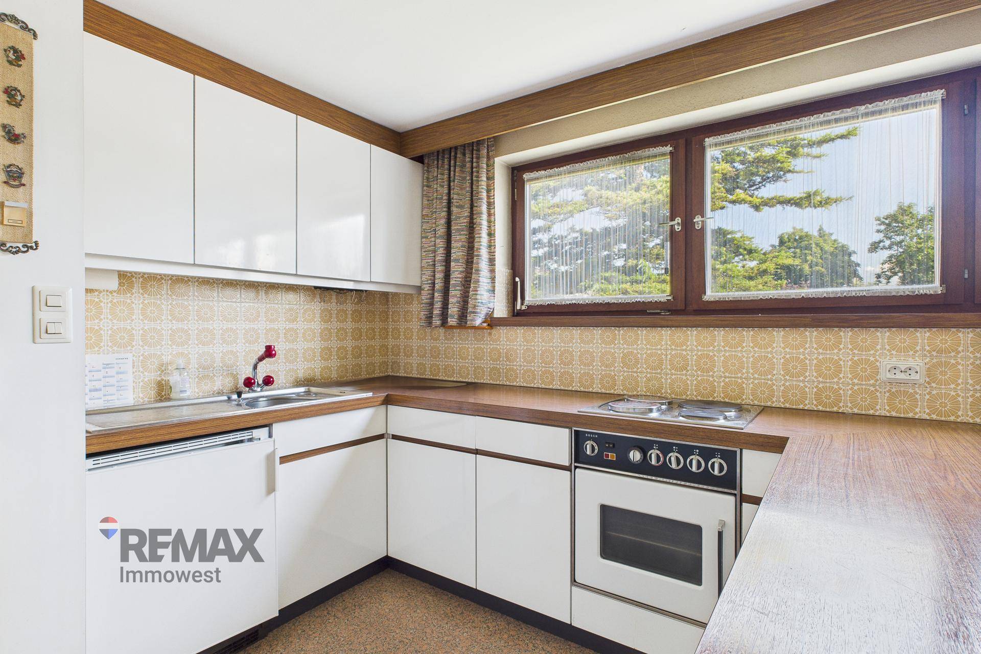 Funktionale Küche im Retro-Stil mit weißen Schränken, Holztheke und Fensterblick.