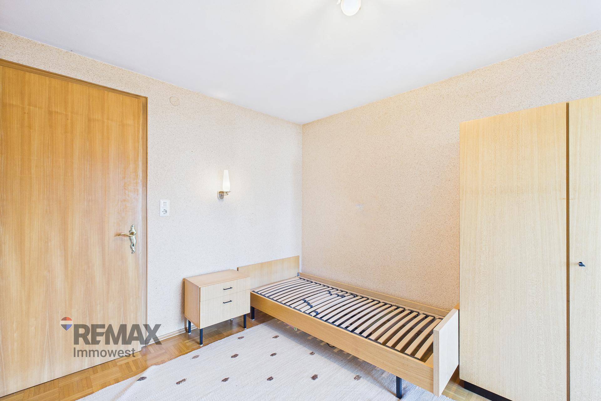 Helles Schlafzimmer mit Einzelbett, Holzmöbeln und schlichtem Design.