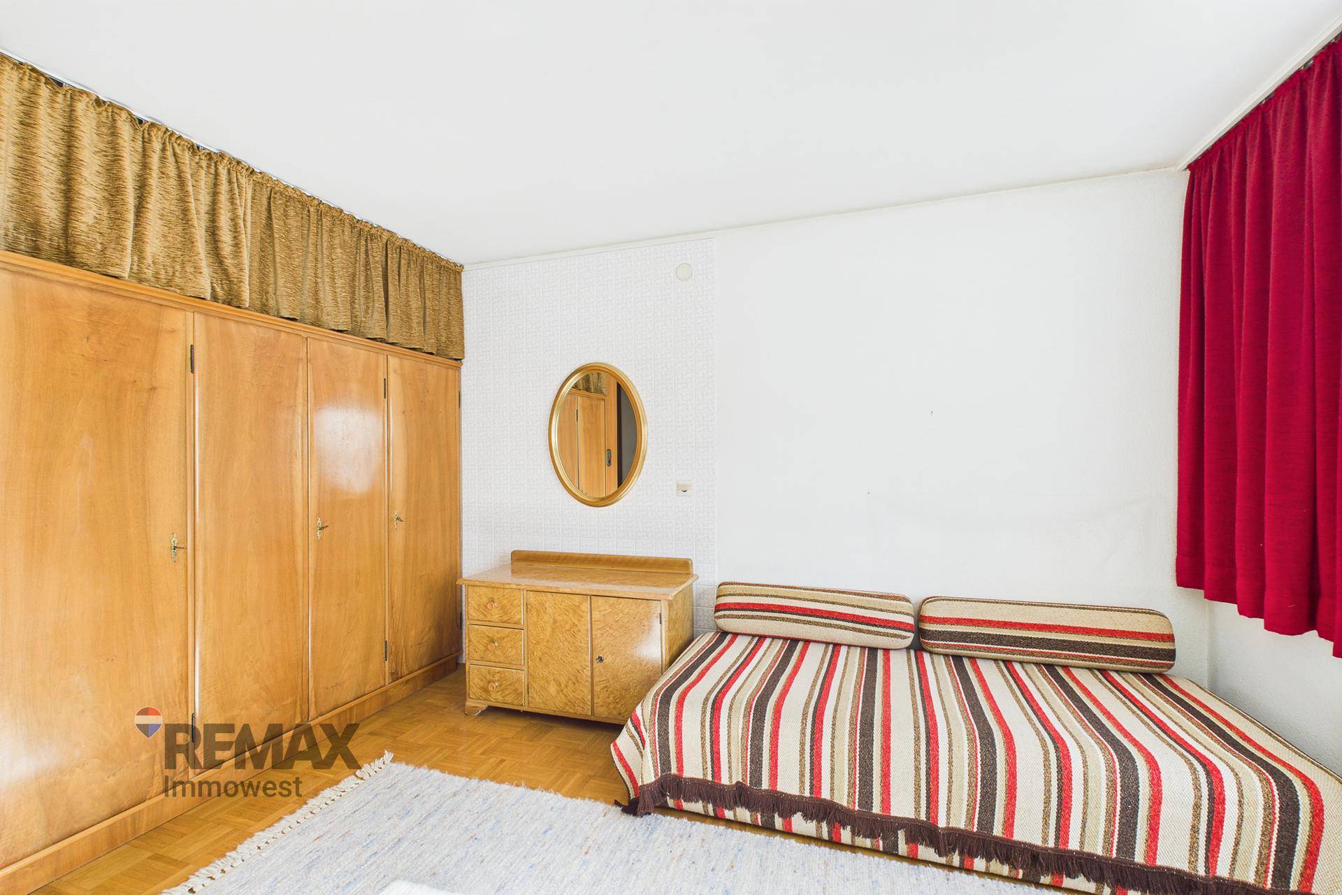 Schlafzimmer mit Holzschrank, Kommode und einem Bett mit gestreifter Tagesdecke.
