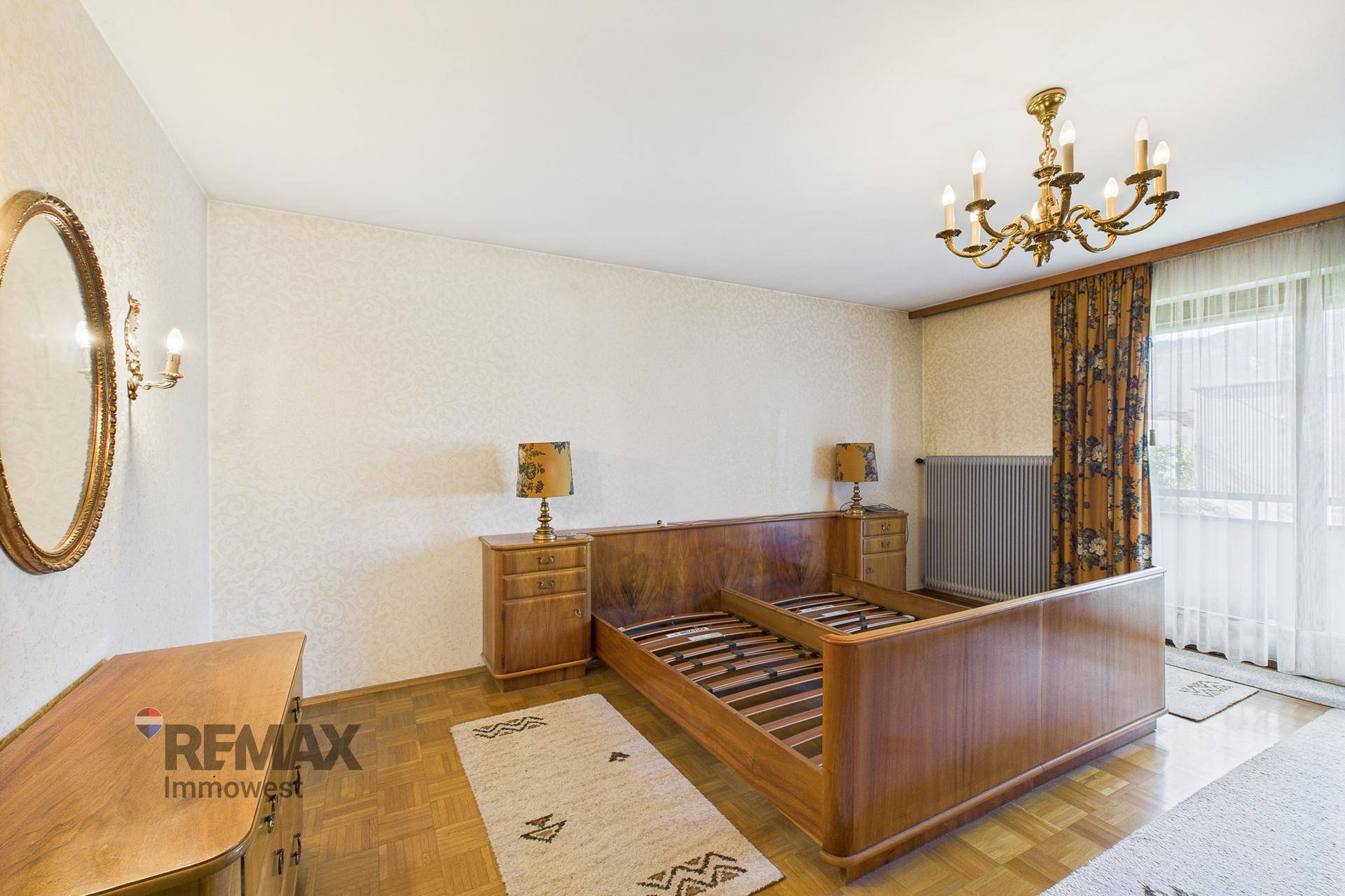 Geräumiges Schlafzimmer mit Doppelbett, Holzparkett und klassischem Kronleuchter.
