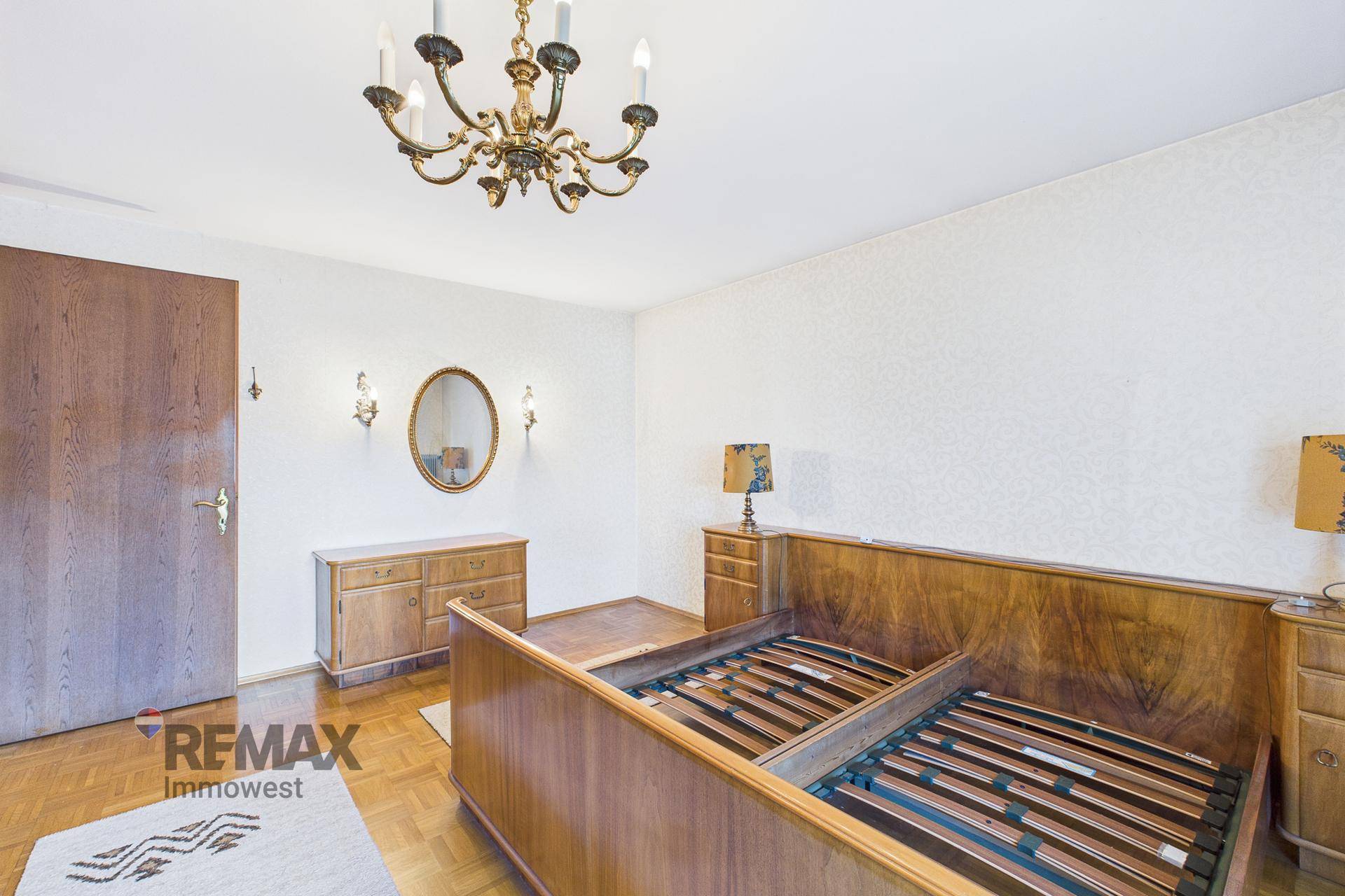 Schlafzimmer mit Holzbettrahmen, passenden Nachttischen und ovalem Spiegel.