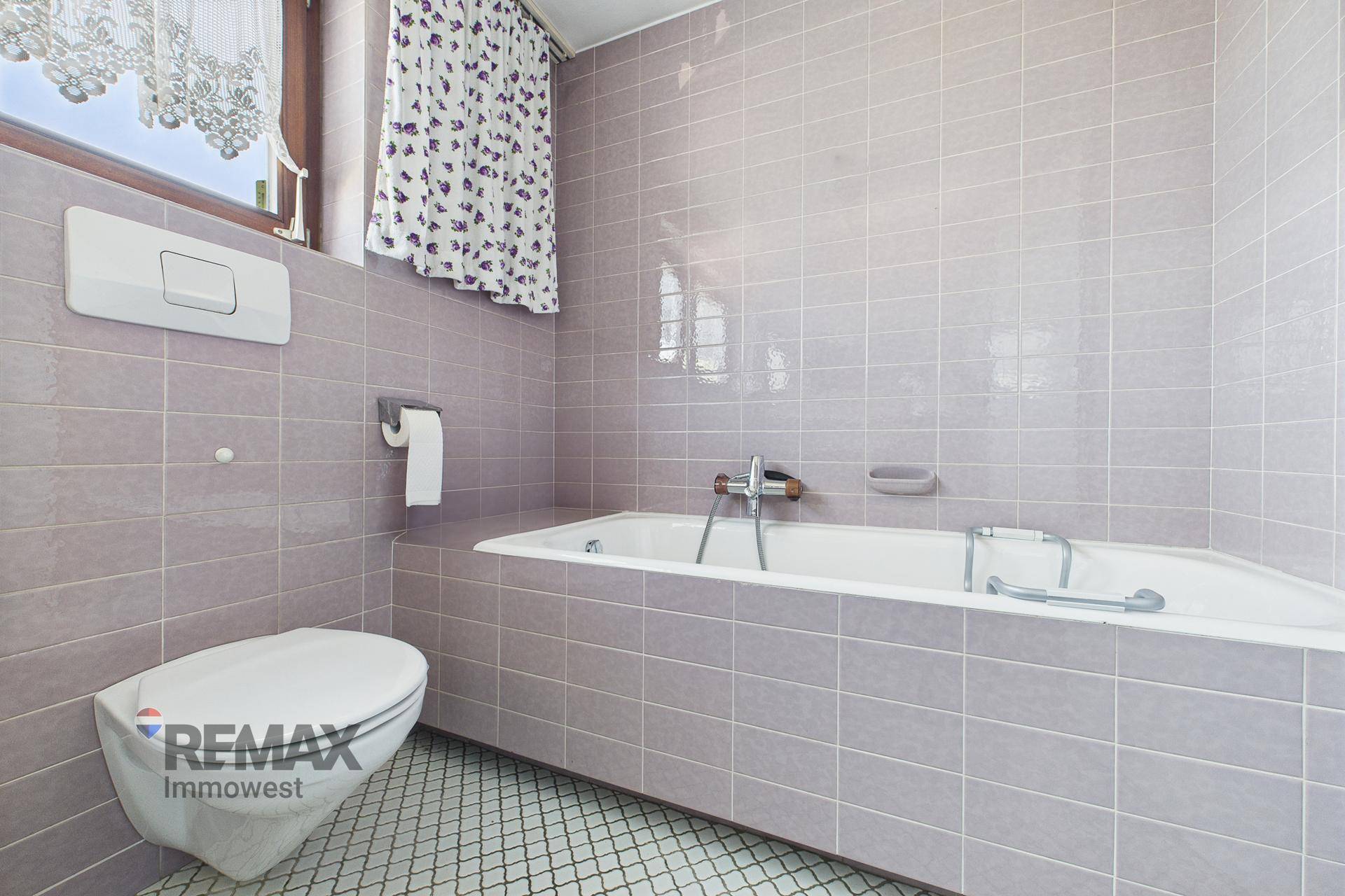 Badezimmer mit Badewanne, WC und rosa Fliesen im Retro-Design.