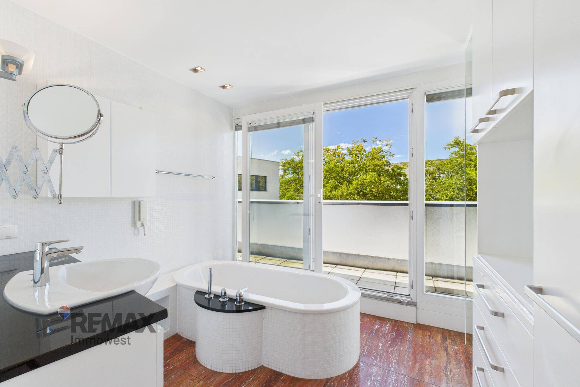 Helles Badezimmer mit freistehender Badewanne und großen Fenstern mit Zugang zur Terrasse.