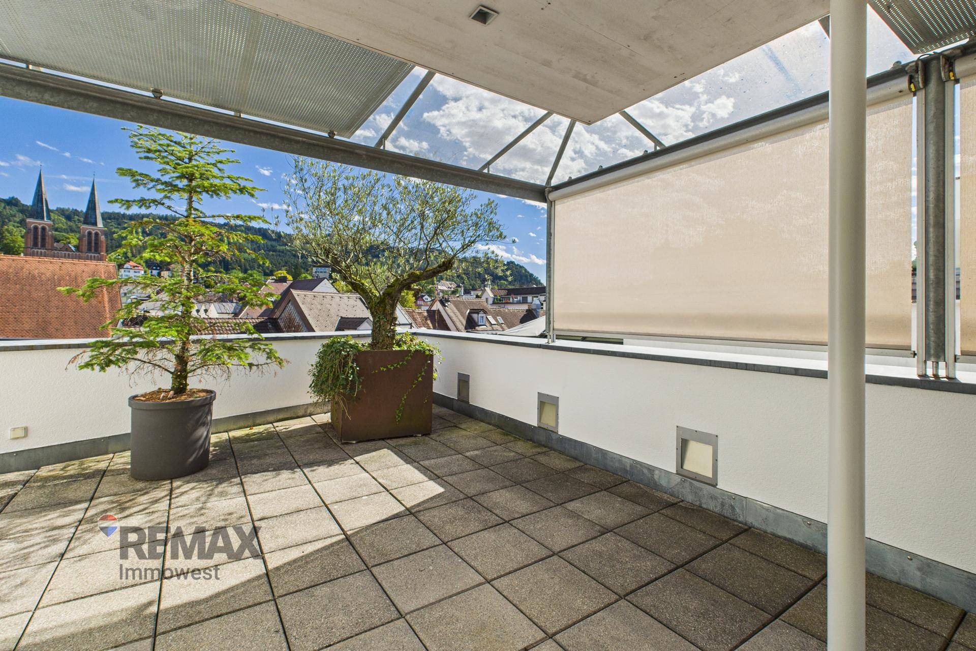 Geräumige Dachterrasse mit Fliesenboden, Pflanzen und Blick über die Dächer der Stadt.