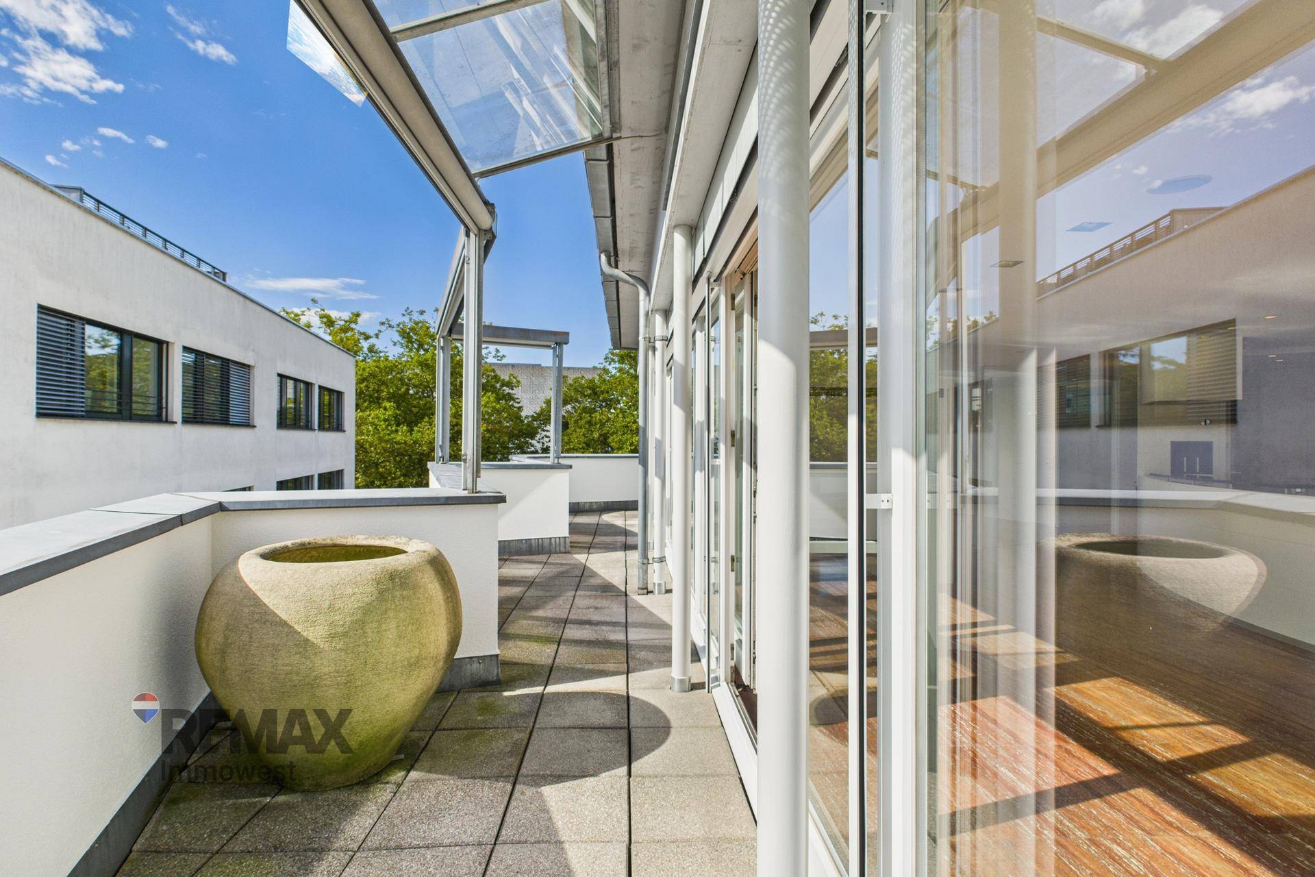 Breite Terrasse mit Fliesenboden und großen Glasfronten, die den Innenbereich mit dem Außenbereich verbinden.