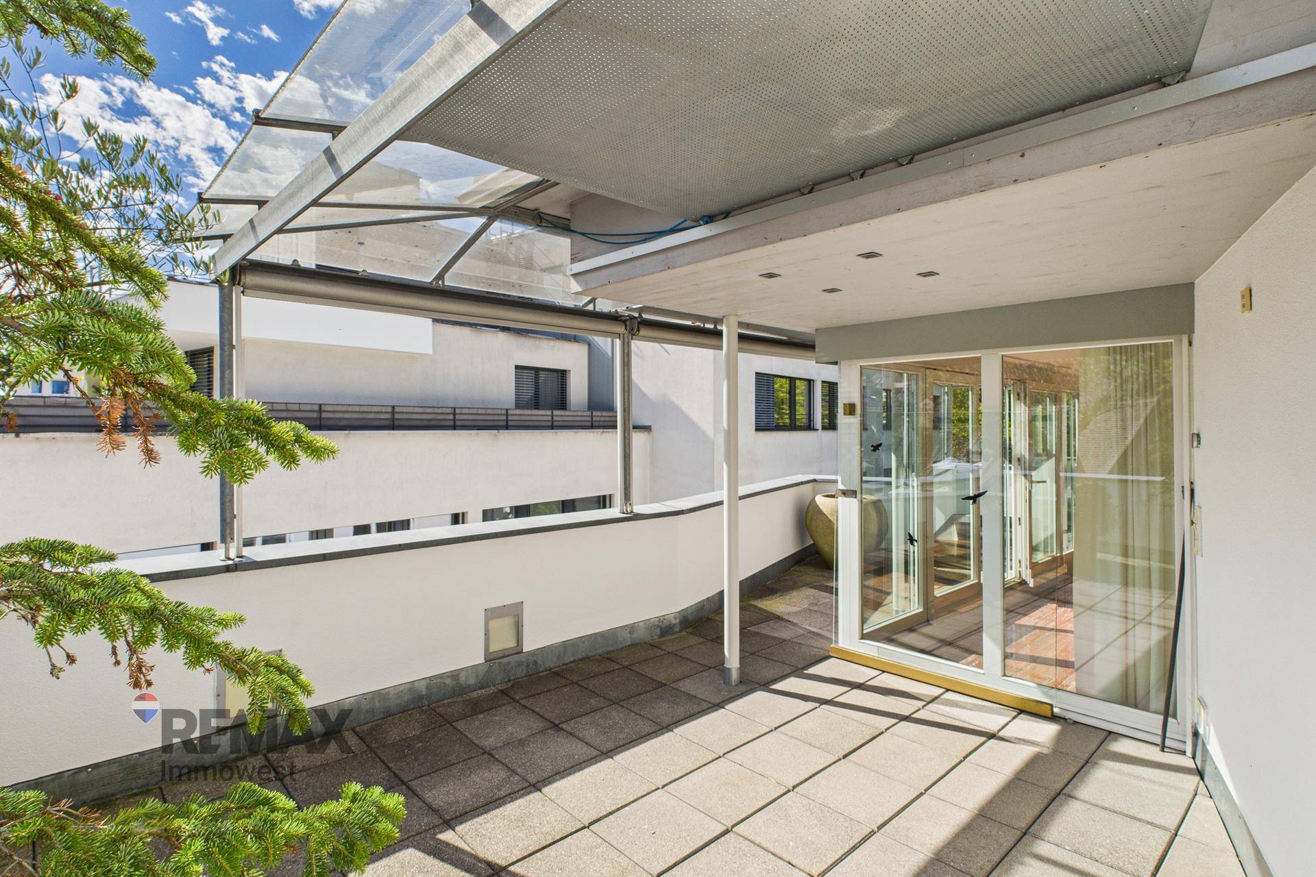 Sonnige Terrasse mit Fliesenboden und Überdachung, die zum Innenbereich des Hauses führt.