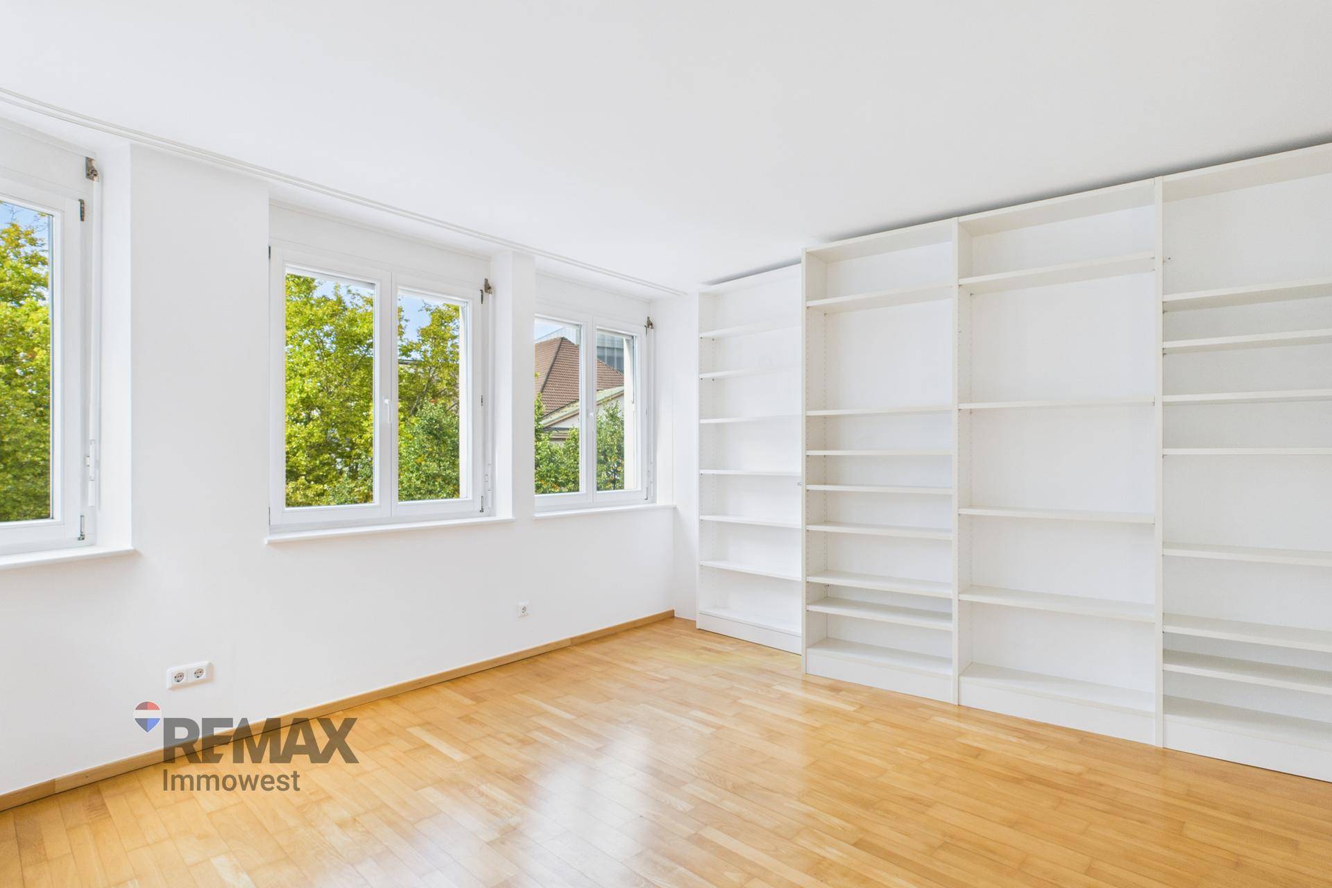 Helles Zimmer mit Holzboden und großen Bücherregalen, ideal als Schlafzimmer oder Arbeitszimmer.