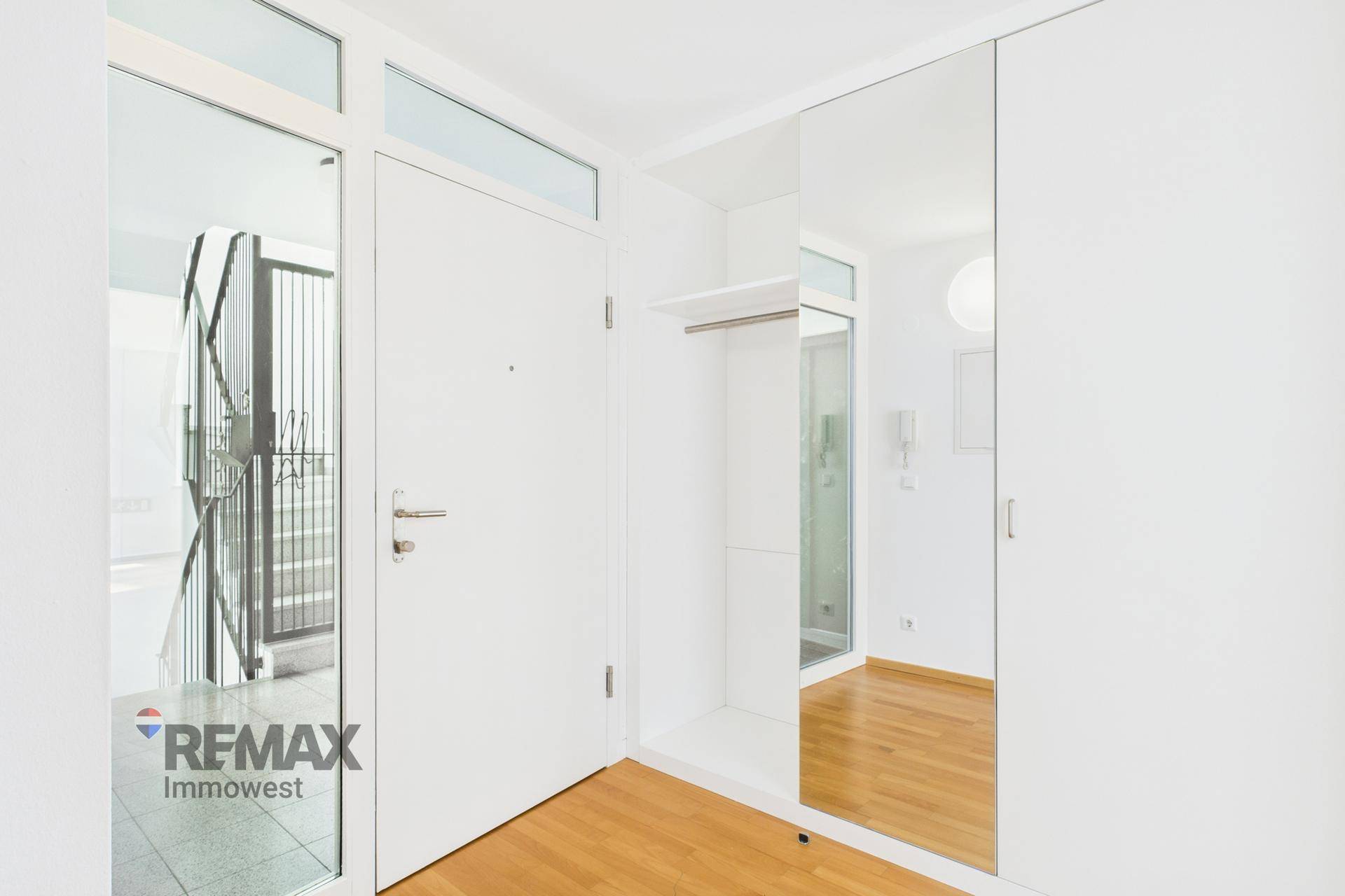 Eingangsbereich mit Spiegelschrank, Holzboden und Zugang zum Treppenhaus in hellem Design.