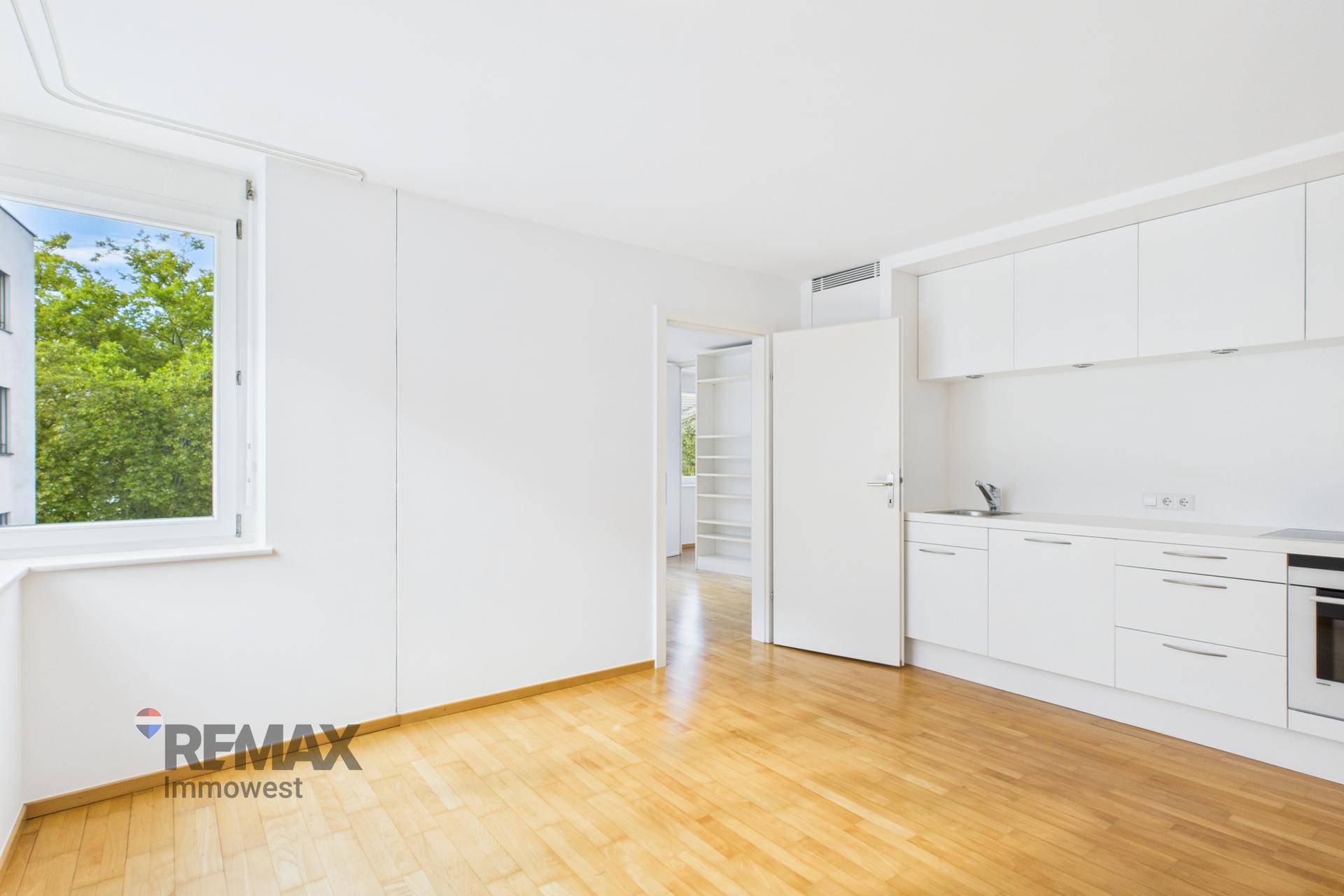 Helle, offene Küche mit weißen Hochglanzschränken und Holzboden in einem modernen Wohnraum.