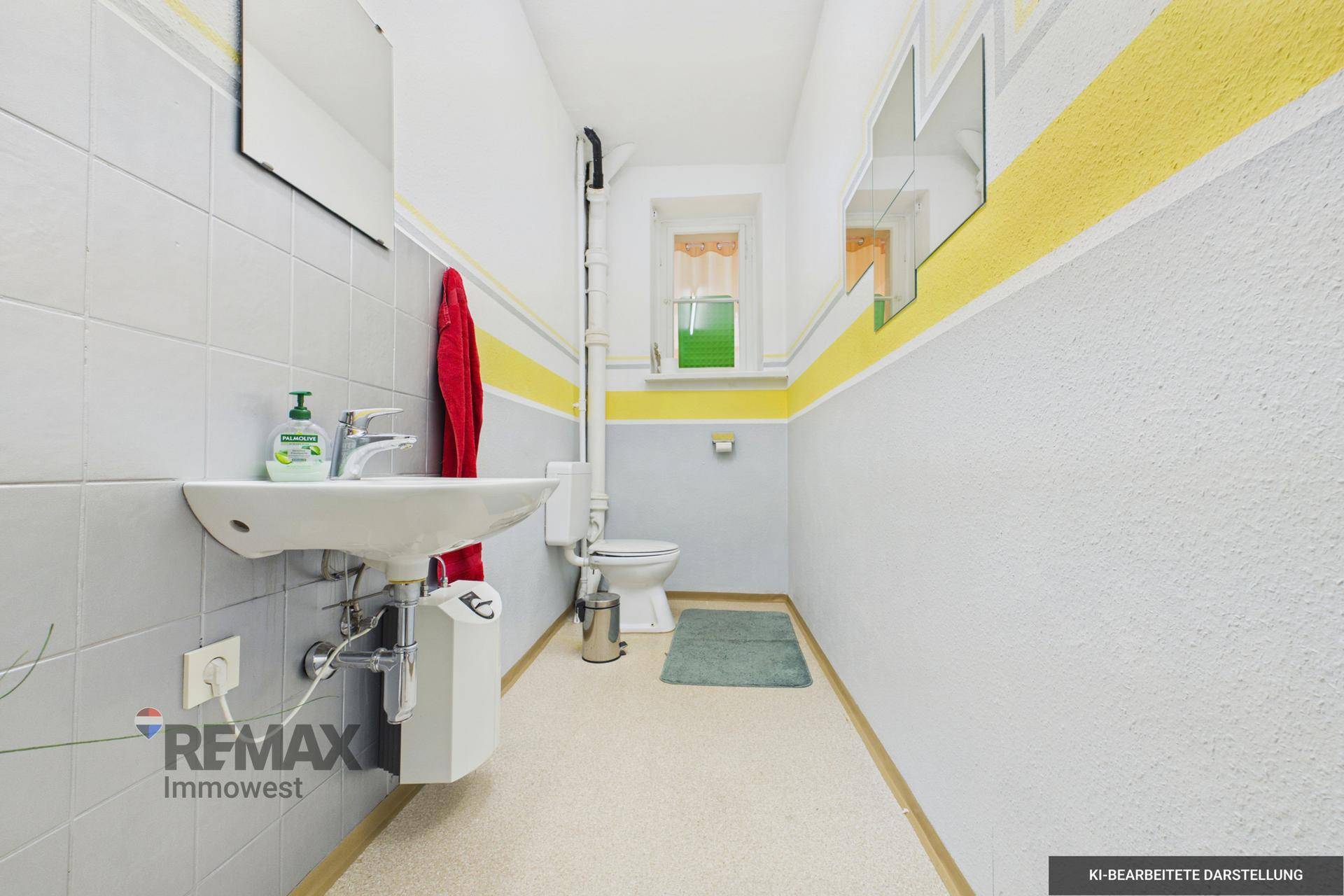 Schlichtes Badezimmer mit grauen Fliesen, WC, Waschbecken und Fenster, funktional gestaltet.