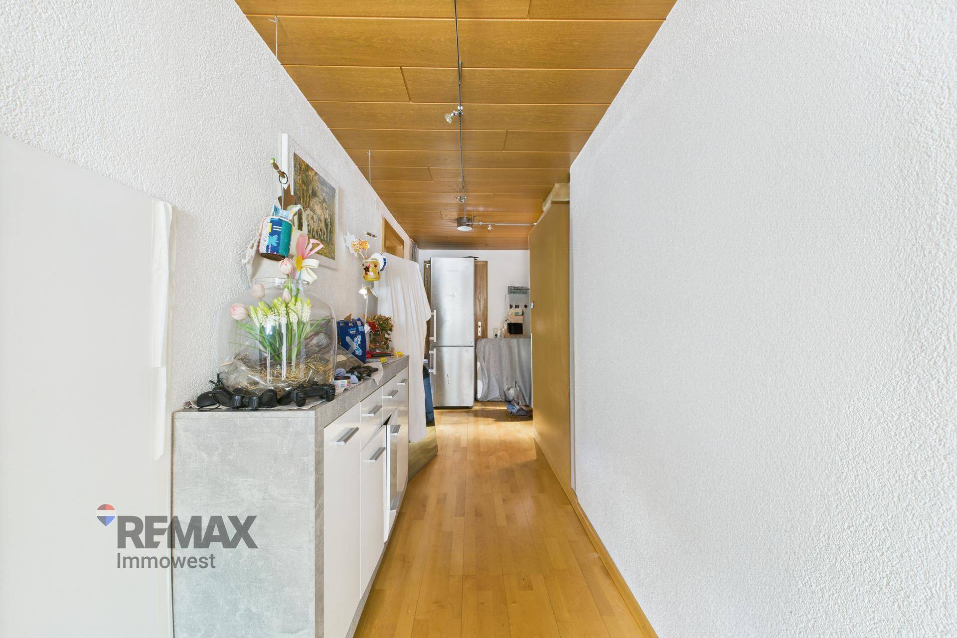 Schmaler Flur mit Holzdeckenpaneelen, hellem Holzboden und einer Ablagefläche.