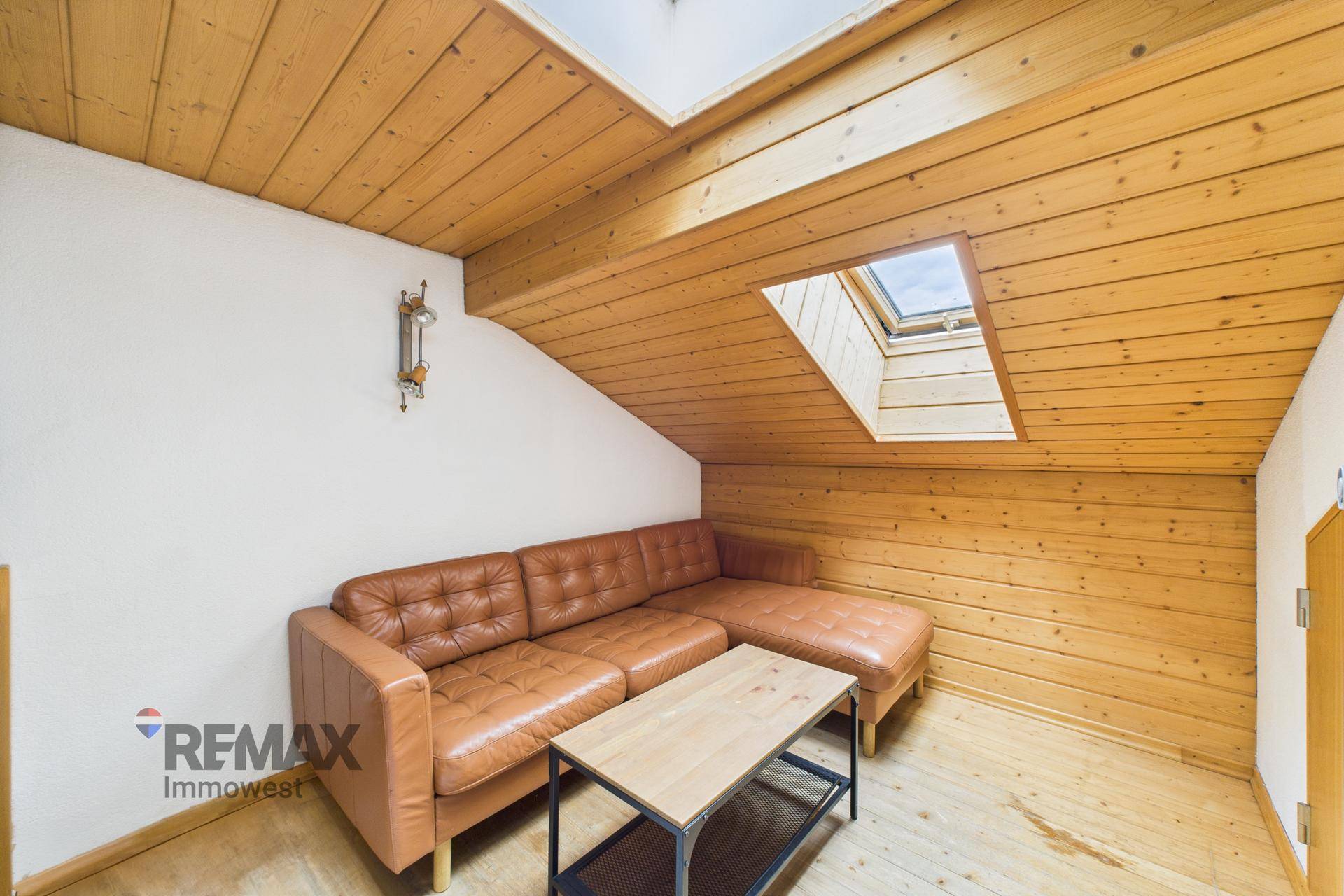 Gemütlicher Dachbodenraum mit Holzverkleidung, Ledersofa und einem Dachfenster für Tageslicht.