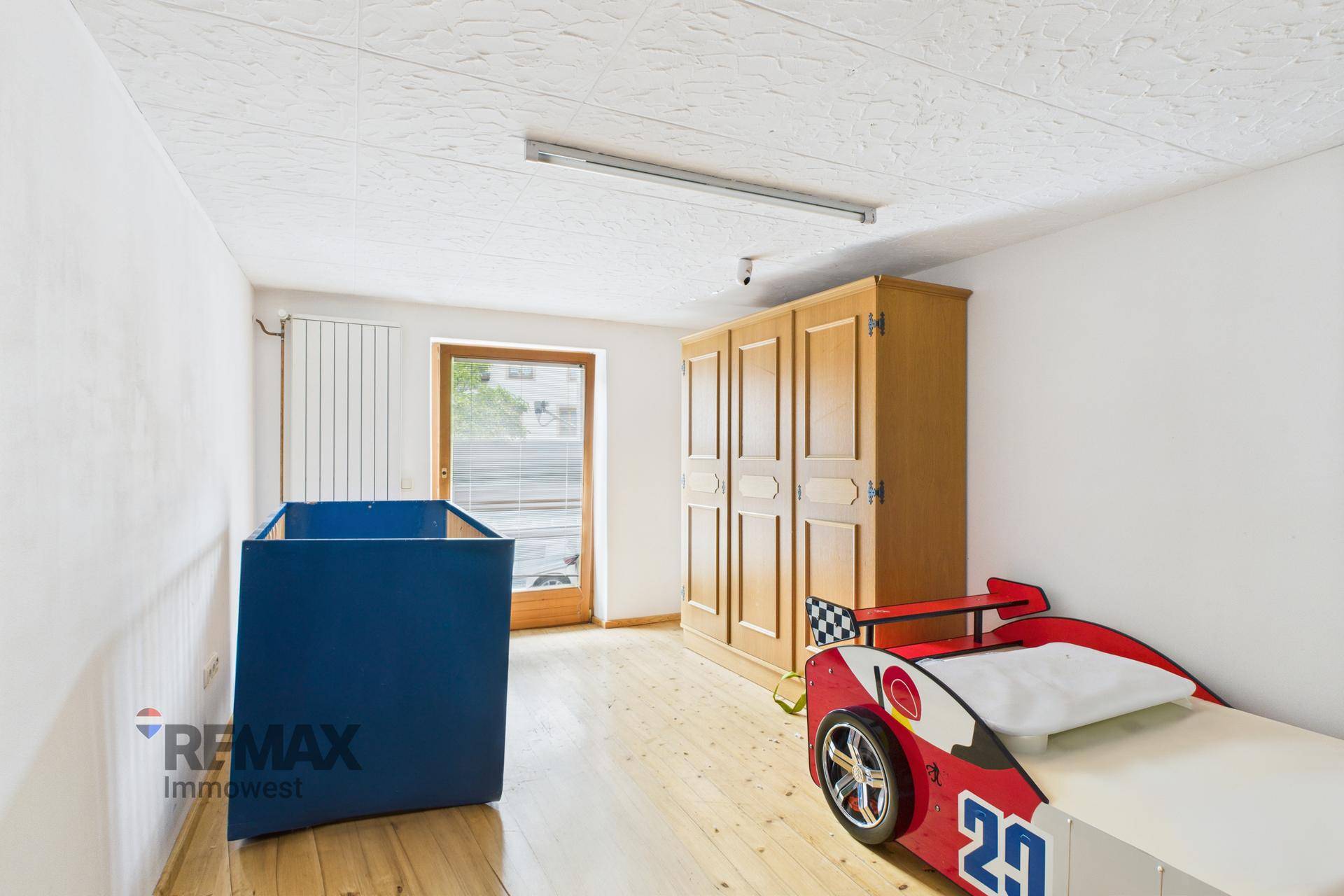 Kinderzimmer mit hellem Holzboden, Holzschrank und einem Rennauto-Bett.