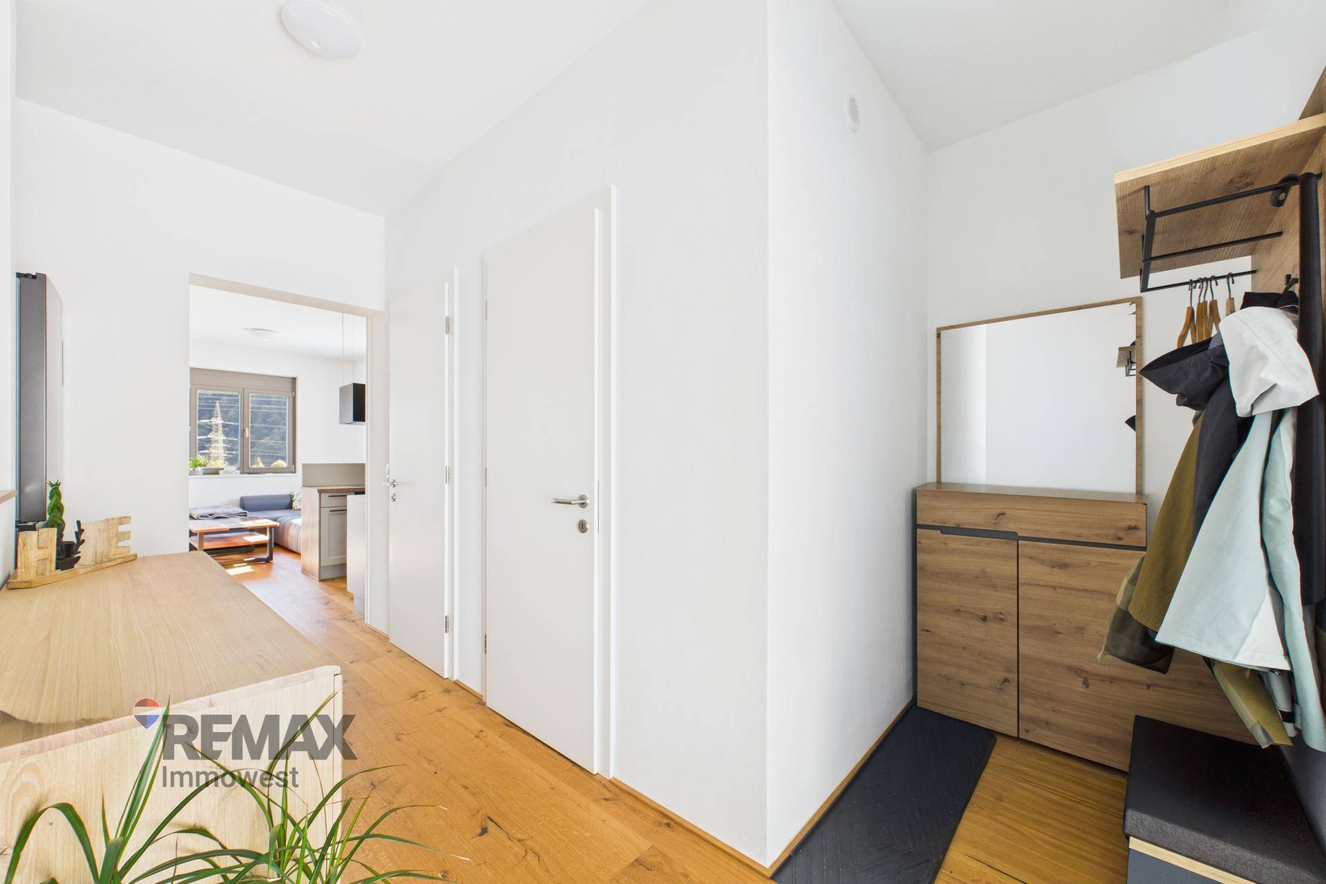 Heller Eingangsbereich mit Holzfußboden und Garderobe, der zu weiteren Räumen führt.