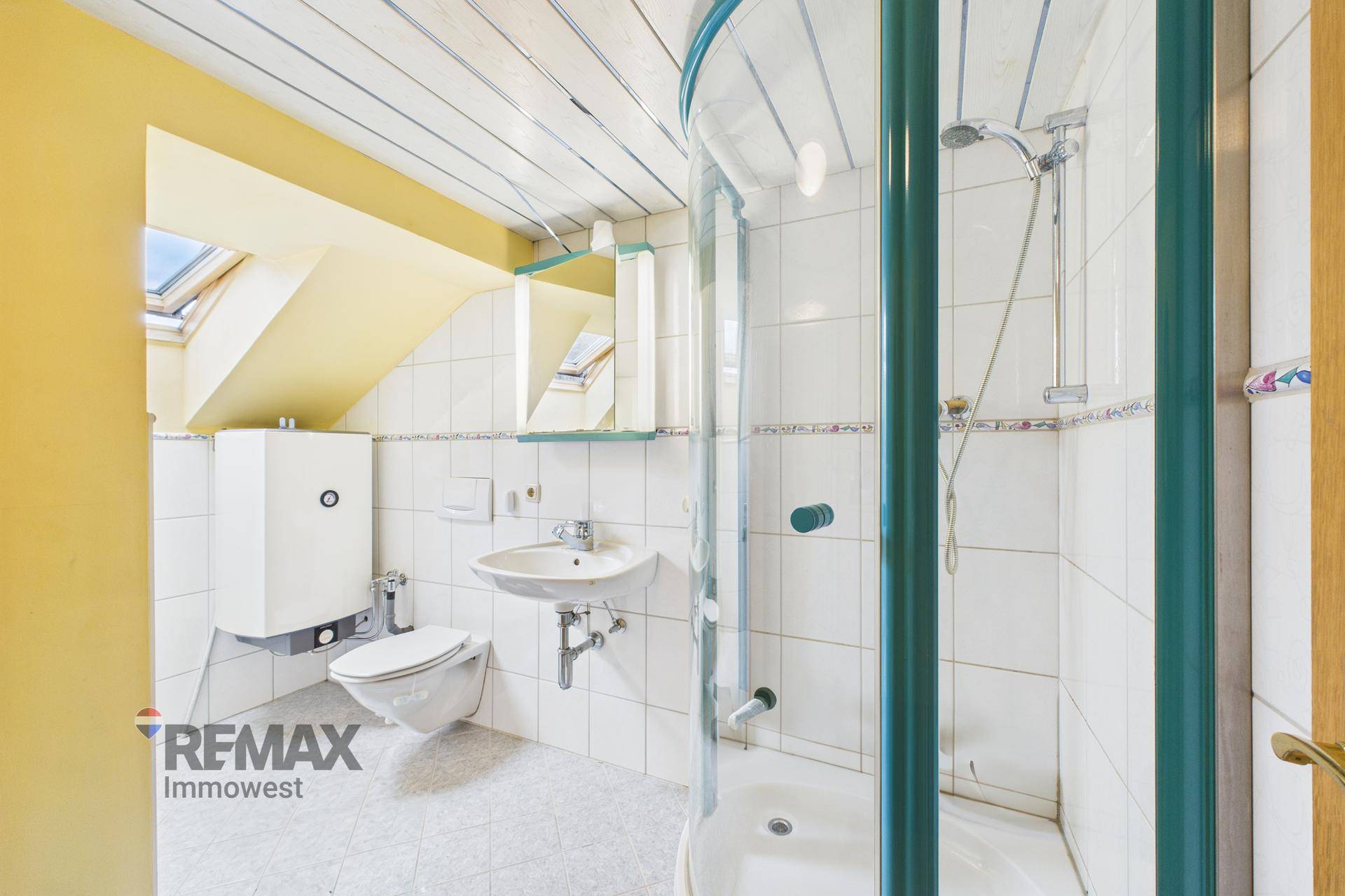 Helles Badezimmer mit Duschkabine, WC, Waschbecken und einem Dachfenster.