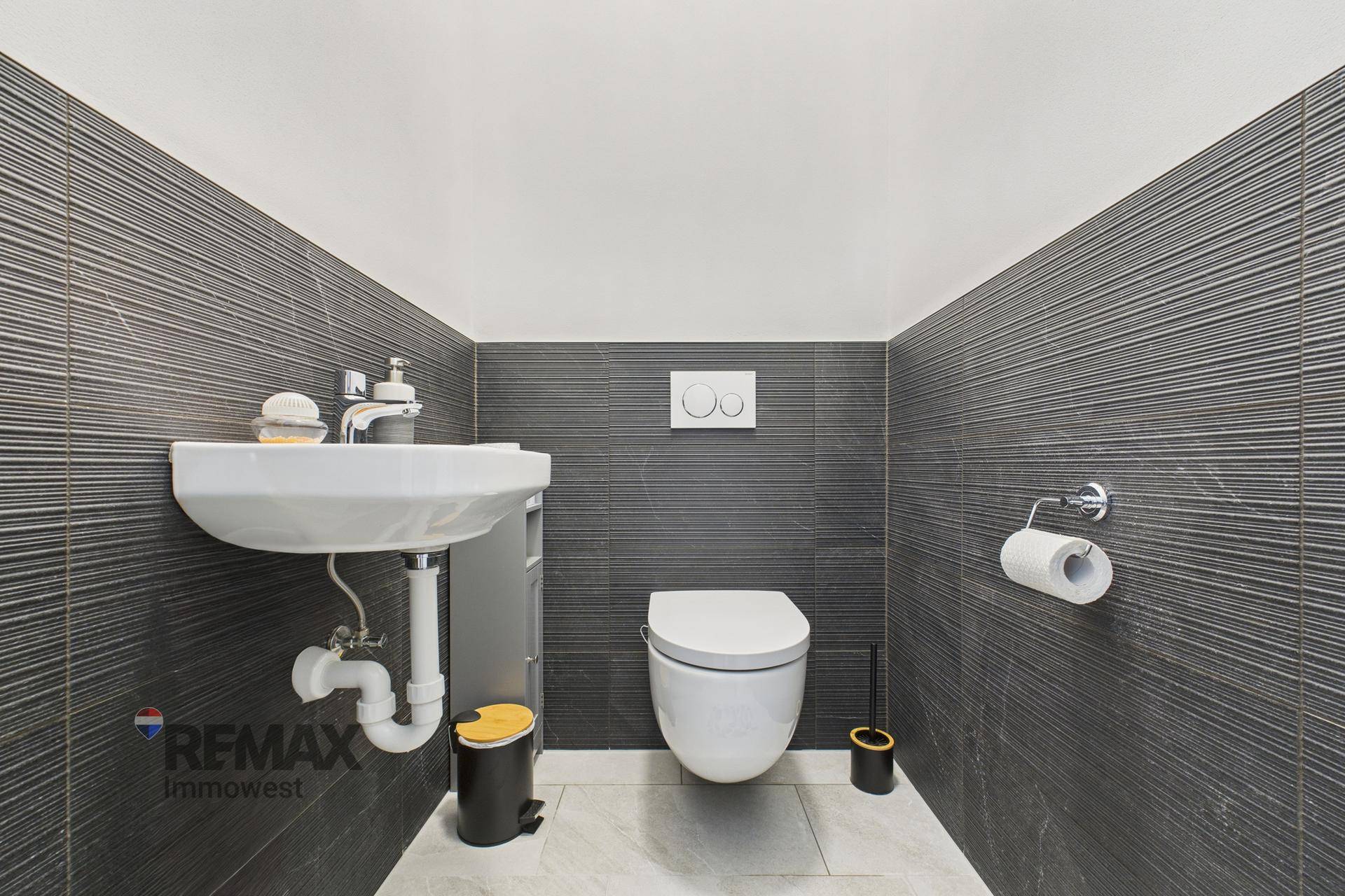 Modernes Gäste-WC mit dunklen strukturierten Fliesen, wandhängendem WC und kleinem Waschbecken.
