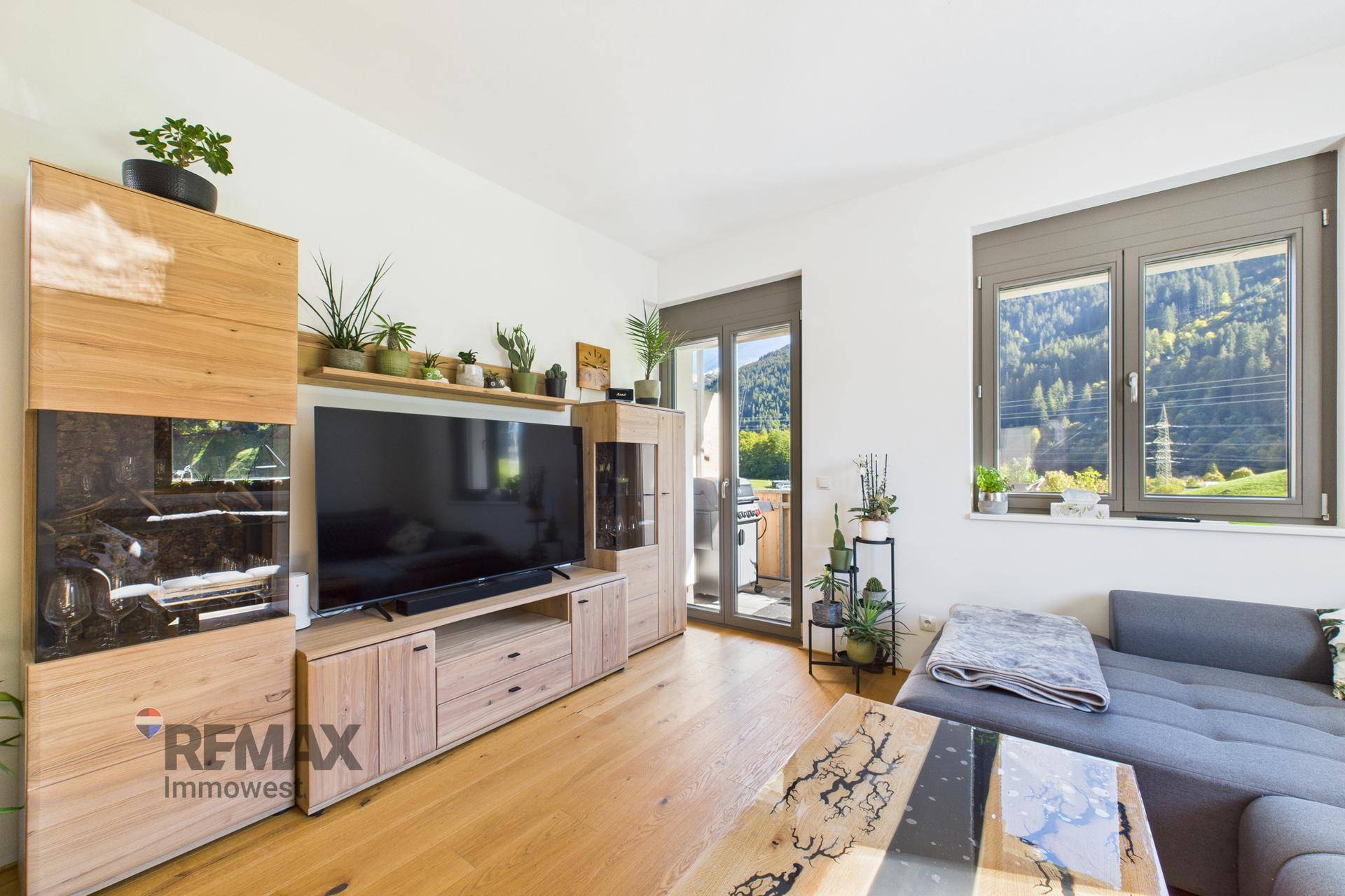 Gemütlicher Wohnbereich mit Sofa und Medienschrank, Zugang zum Balkon und Bergblick.