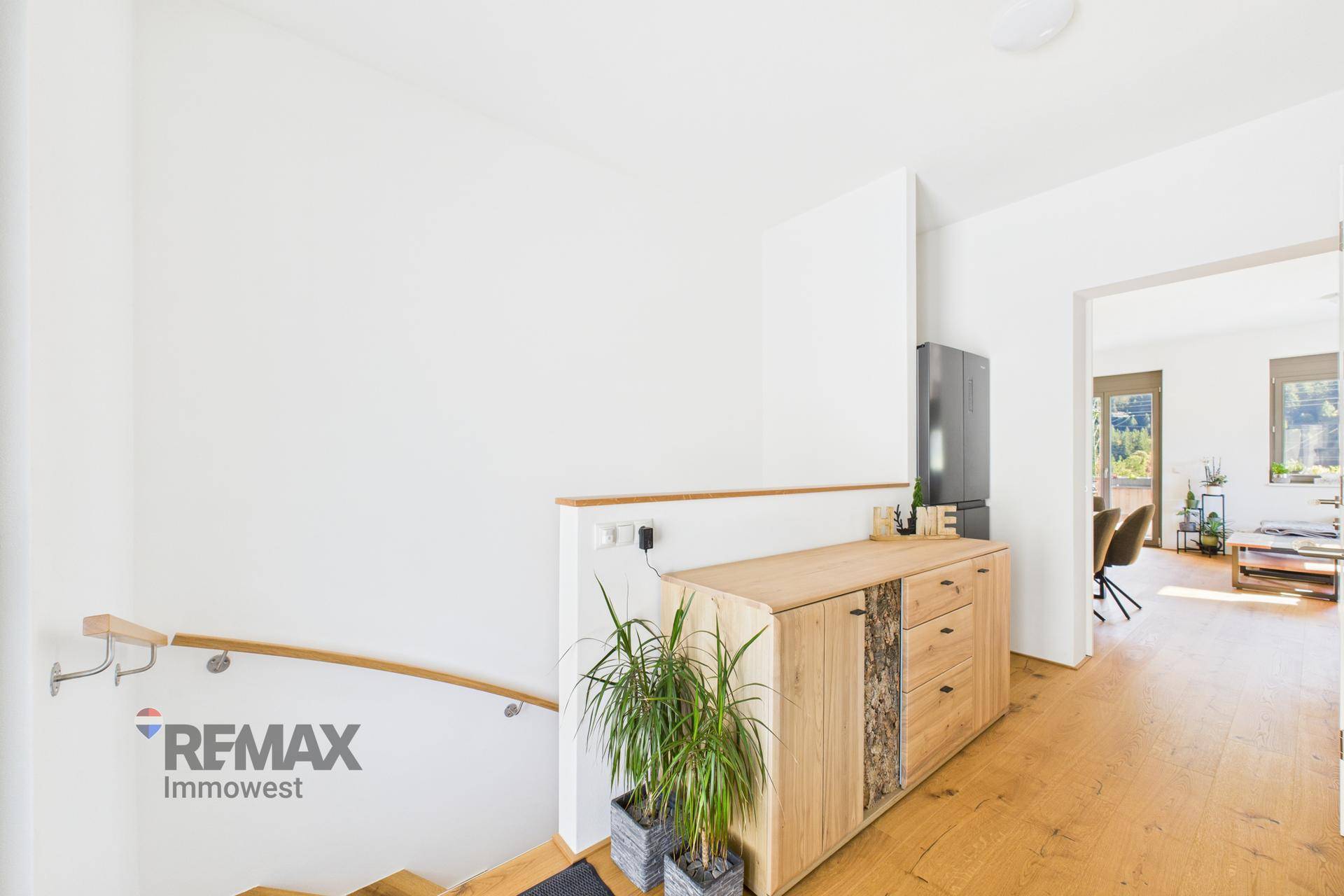 Heller Flur mit Holzkommode und Zugang zu einer Holztreppe, die in eine andere Etage führt.