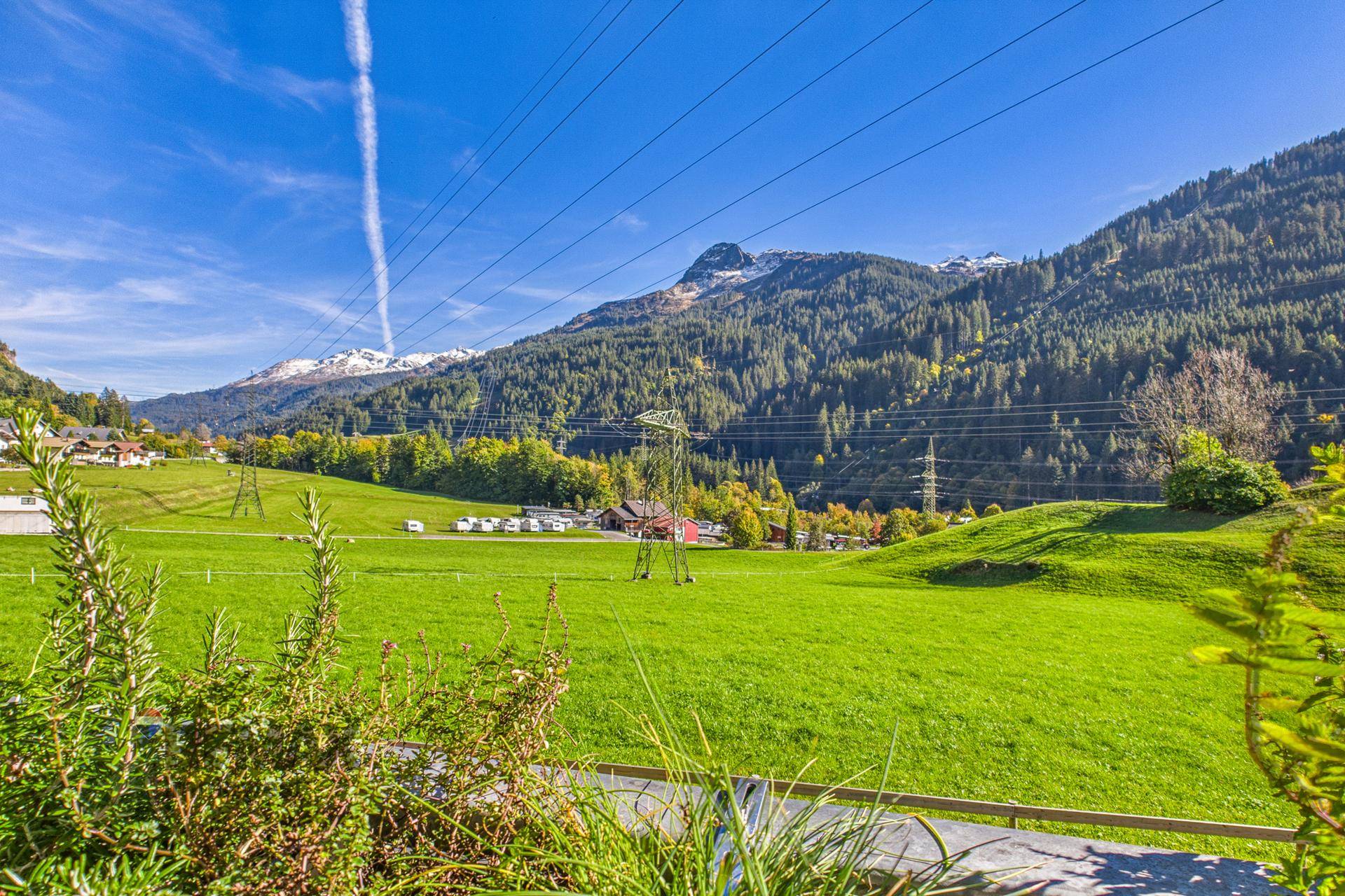 Weite grüne Wiesen und bewaldete Berge unter strahlend blauem Himmel, idyllische Landschaft.
